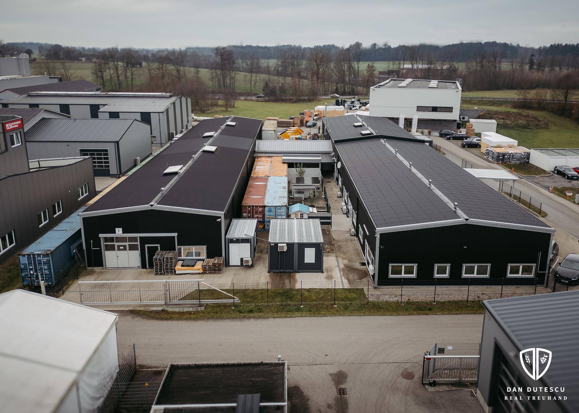 Luftbild des Gewerbeareals mit verschiedenen Gebäuden, Lagerflächen und der angrenzenden ländlichen Umgebung.