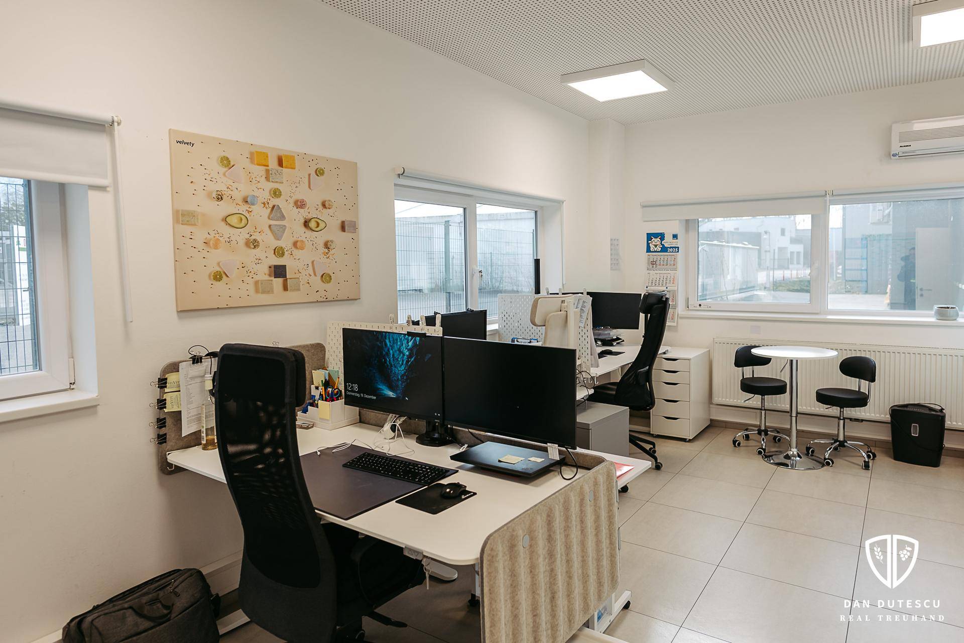 Modernes Großraumbüro mit mehreren Arbeitsplätzen, Computern und großen Fenstern für viel Tageslicht.