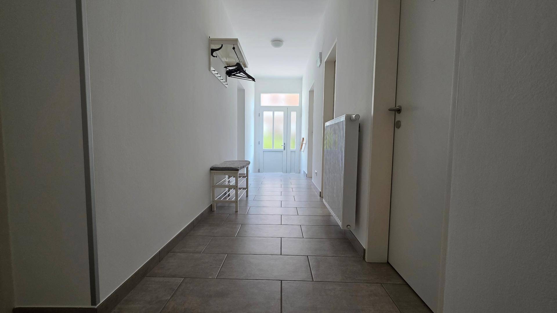 Langer Flur mit Fliesenboden, Garderobe und Blick zur Eingangstür, hell und einladend.