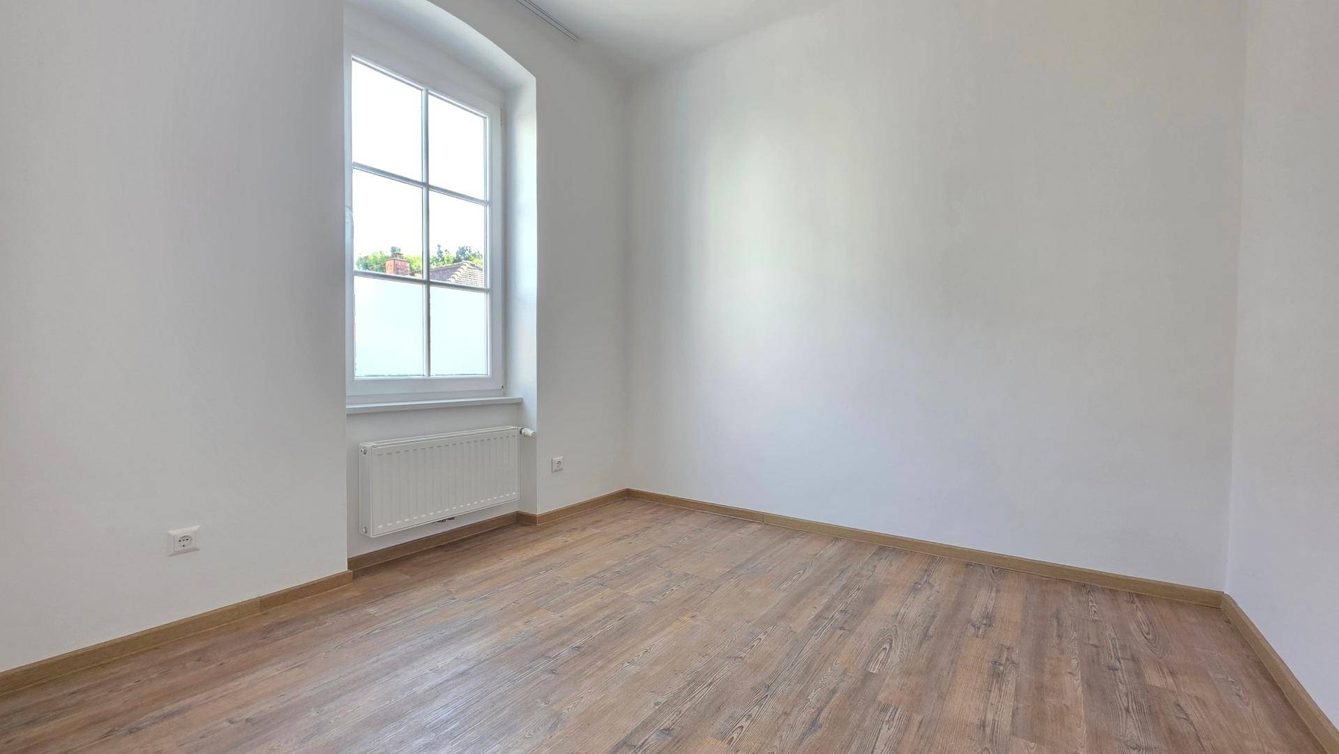 Helles Zimmer mit Laminatboden und einem Fenster, das viel Tageslicht spendet, ideal als Schlafzimmer.