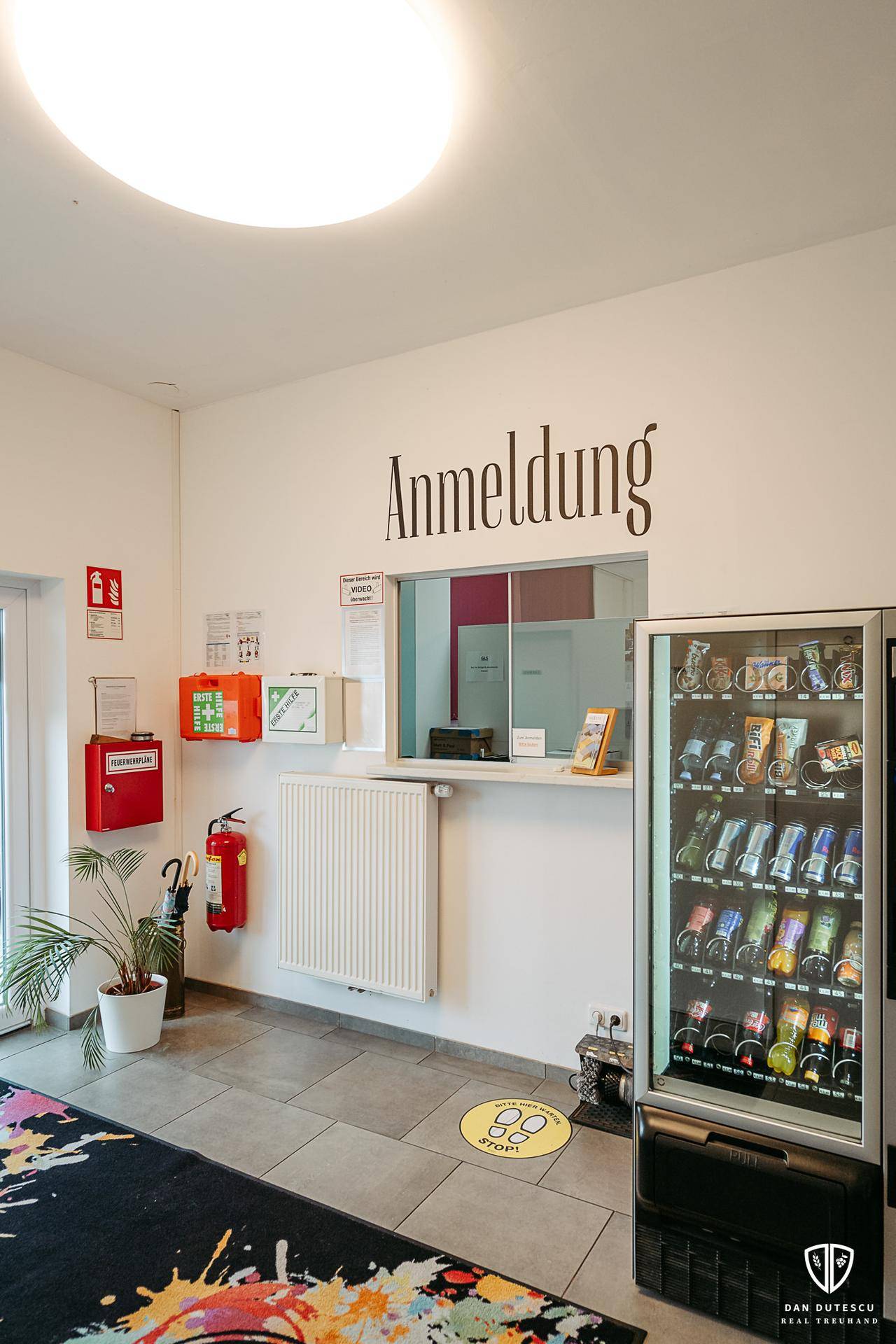 Empfangsbereich mit Anmeldeschalter, Verkaufsautomat und Sicherheitsausrüstung an der Wand.