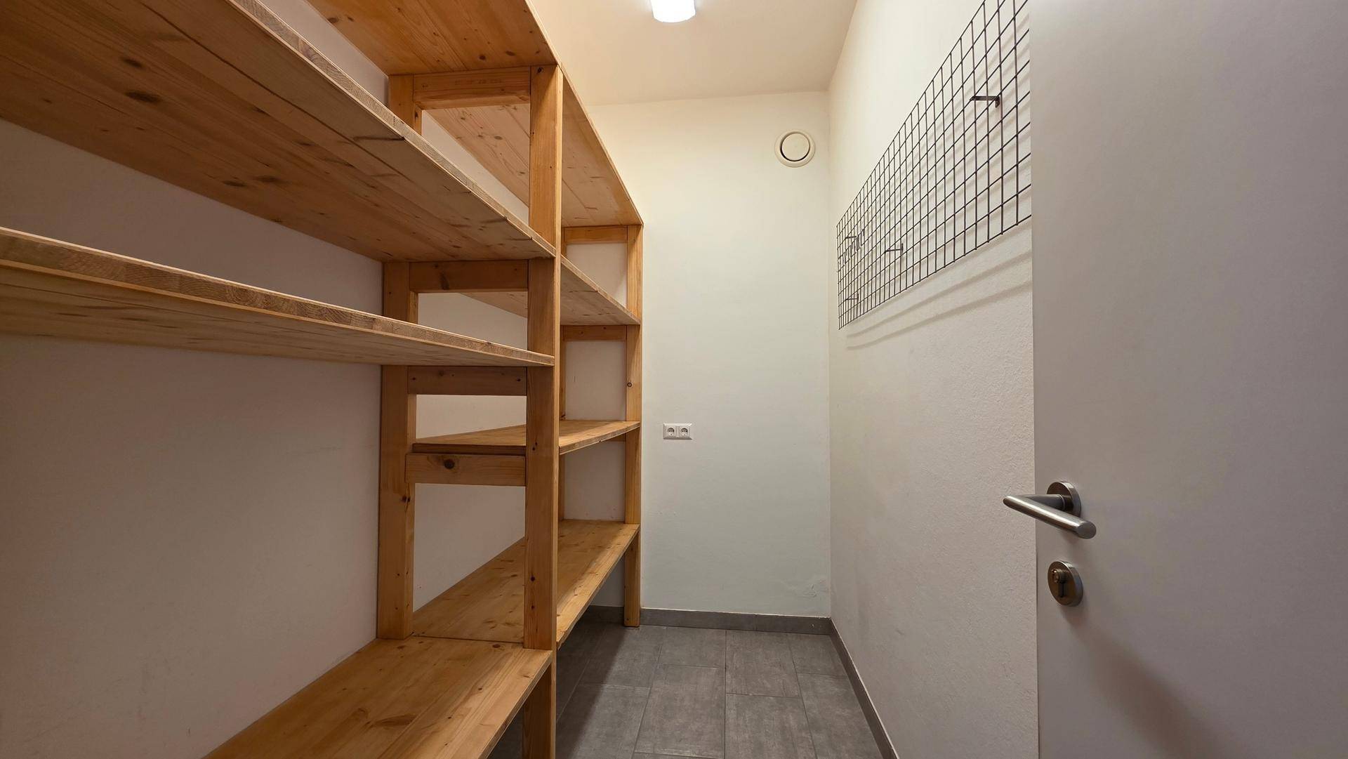 Praktischer Abstellraum mit Holzregalen und Fliesenboden für zusätzlichen Stauraum und Organisation.