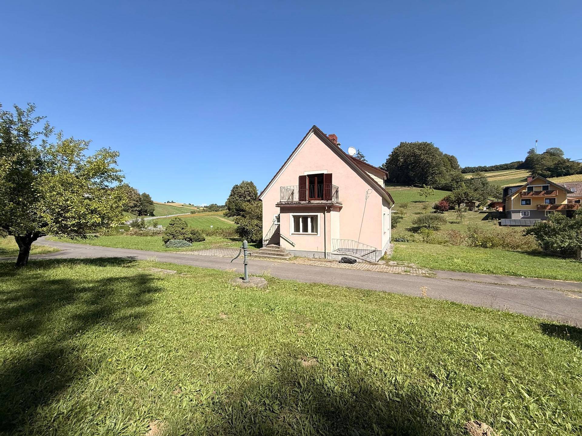 Charmantes Einfamilienhaus mit Balkon und gepflegtem Vorgarten, umgeben von grüner Natur.