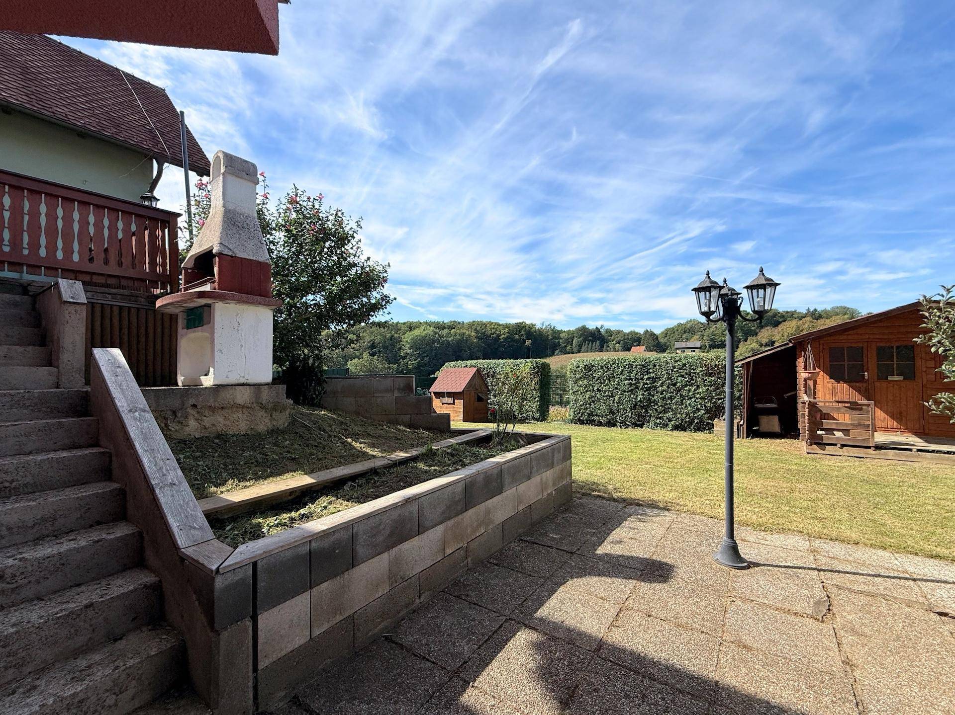 Gepflegter Garten mit Rasenfläche, Gartenhaus und gemauertem Grill.