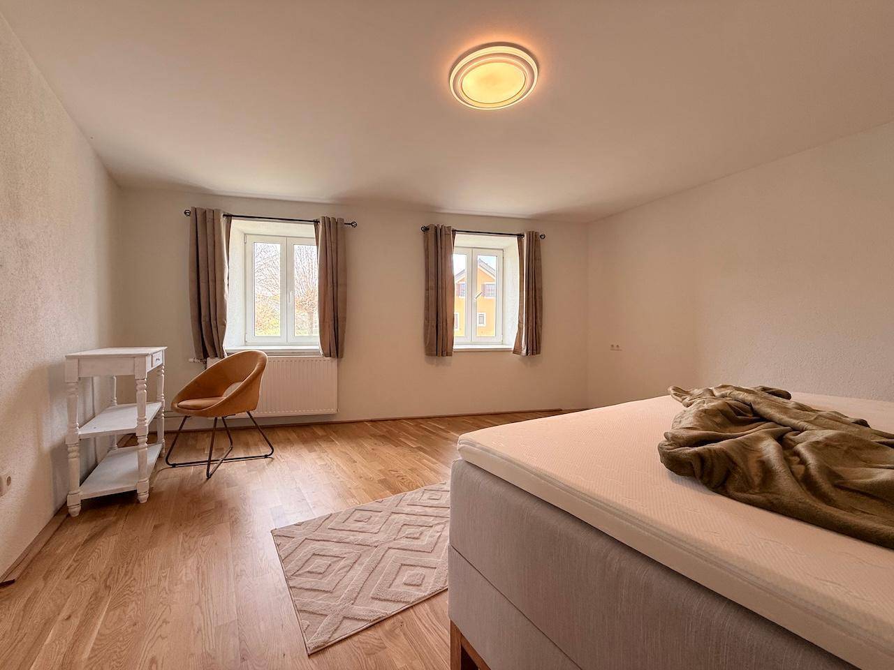 Helles Schlafzimmer mit Holzboden und zwei Fenstern für viel Tageslicht.