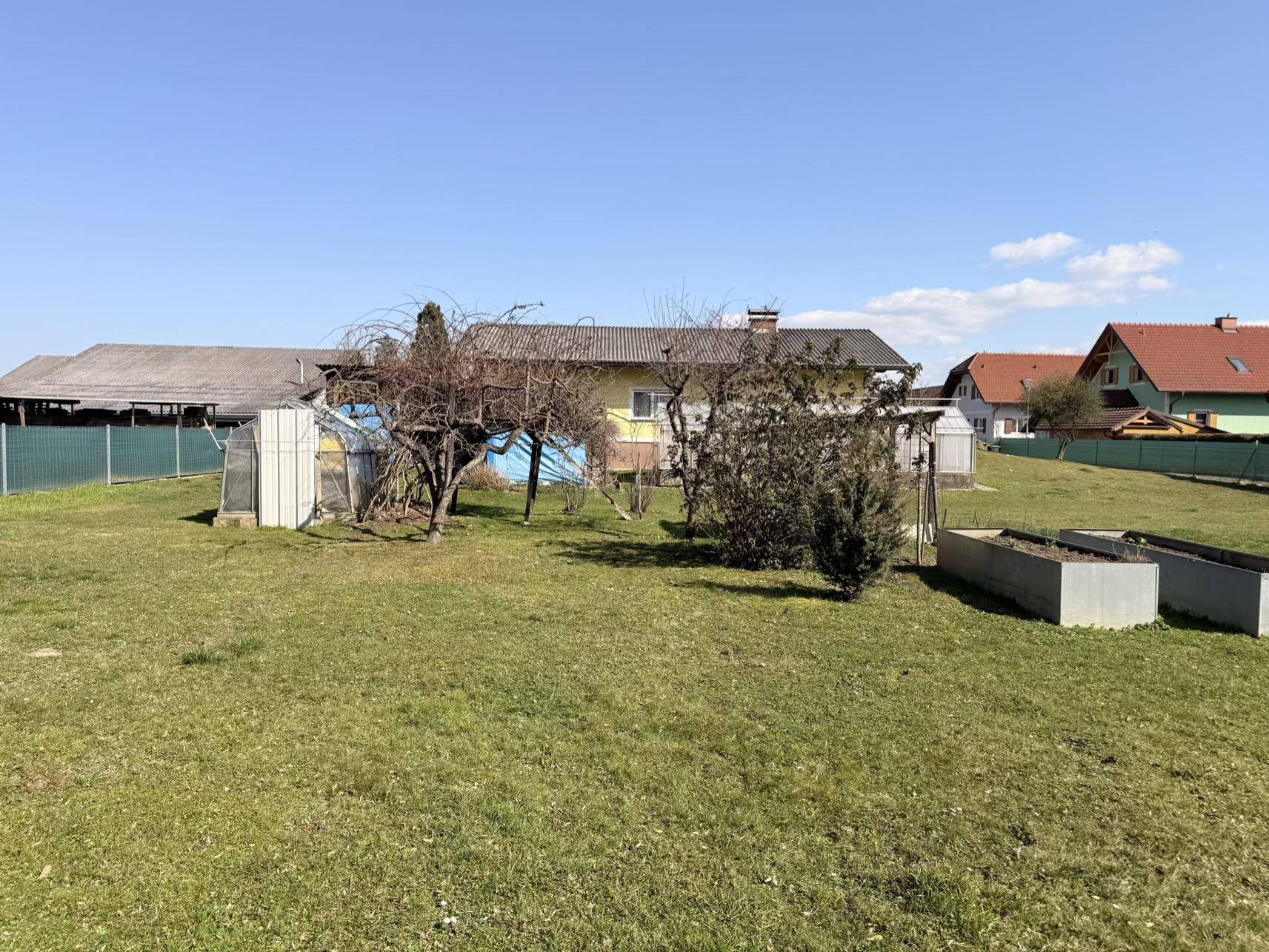Großer Gartenbereich mit Hochbeeten und dem Haus im Hintergrund, umgeben von einer grünen Rasenfläche.