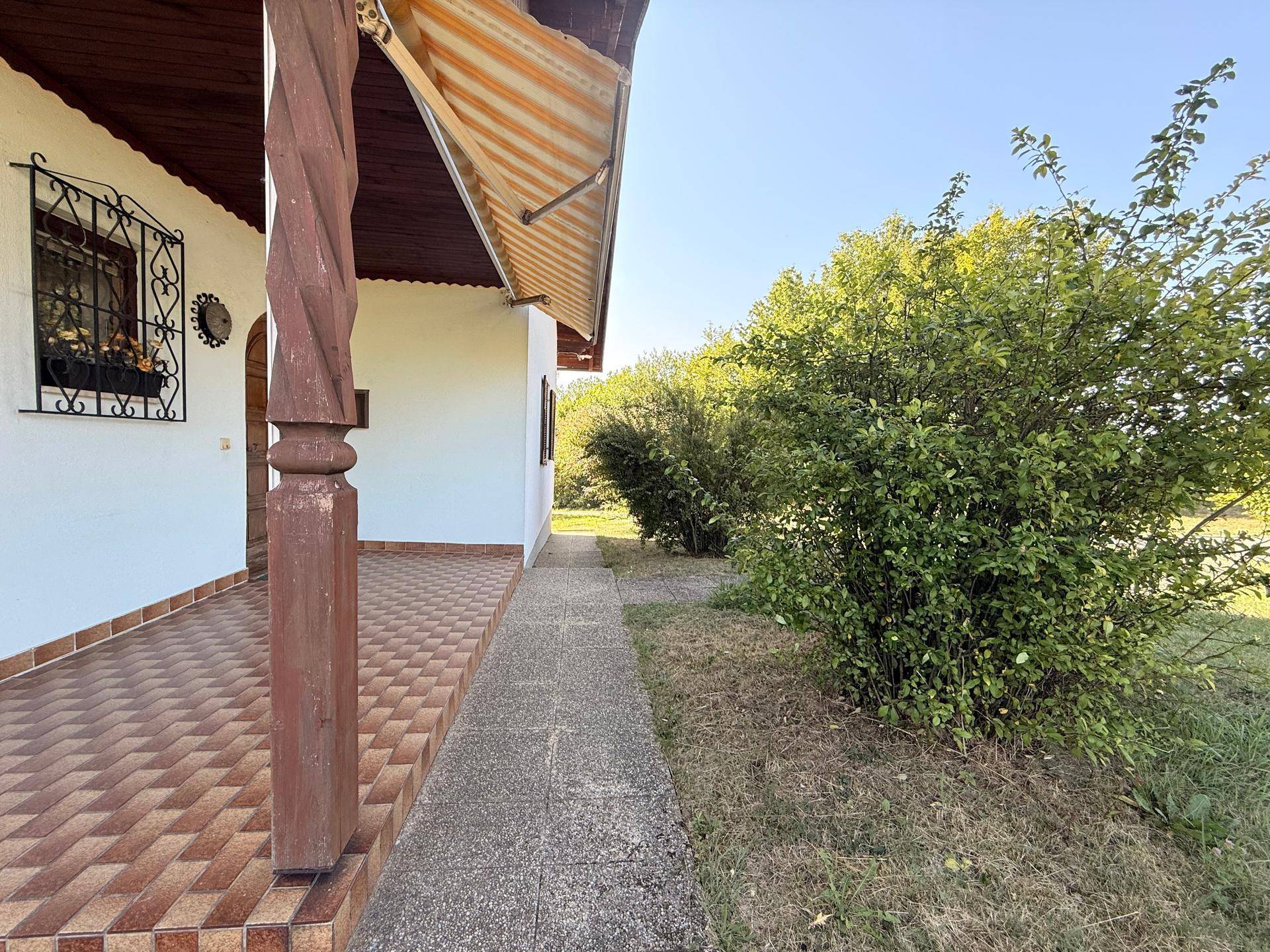 Überdachte Terrasse an der Seite des Hauses mit Fliesenboden und rustikalen Holzpfeilern.
