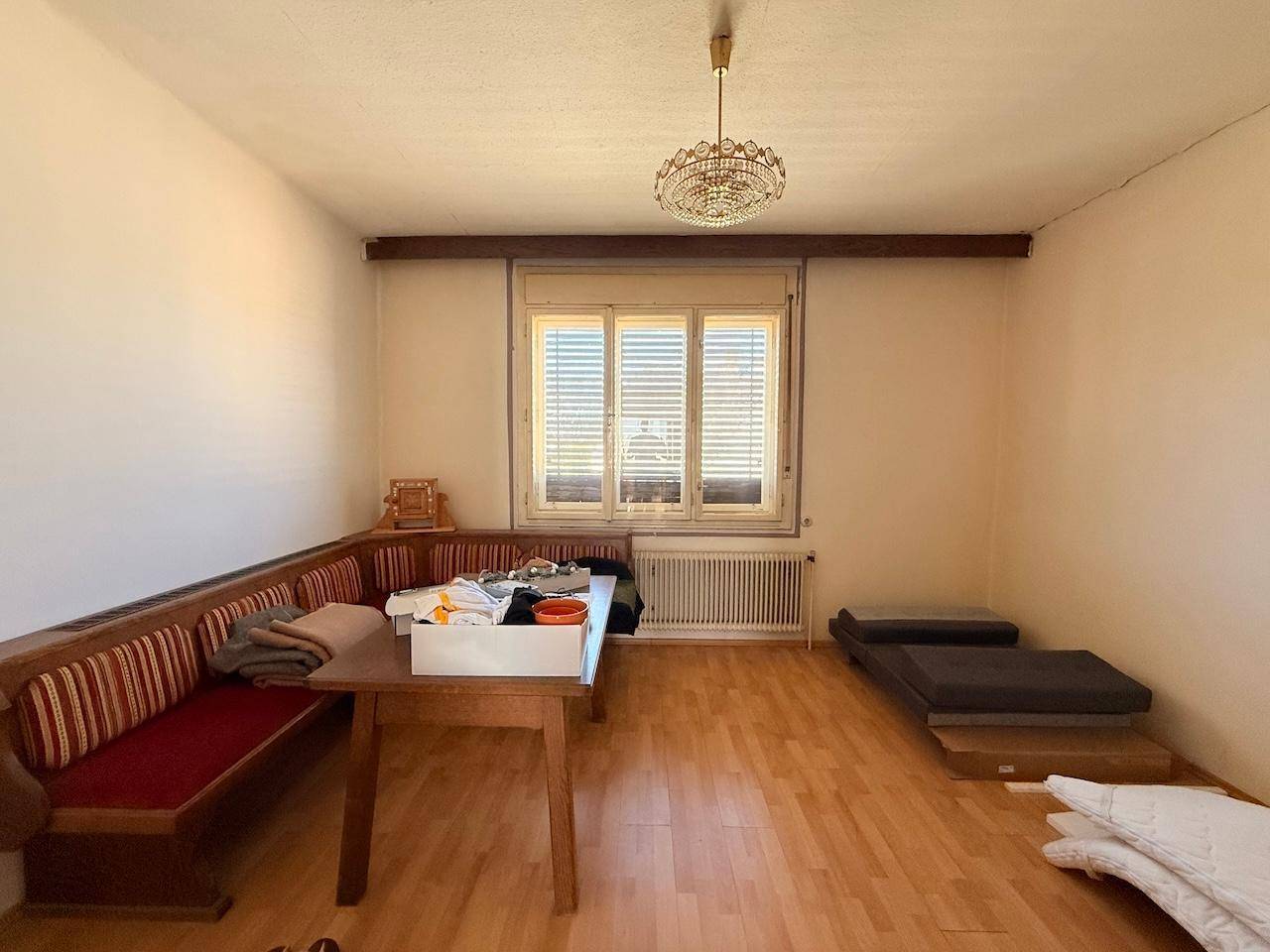 Raum mit traditioneller Eckbank, Holztisch und Fenster, in ursprünglichem Zustand.