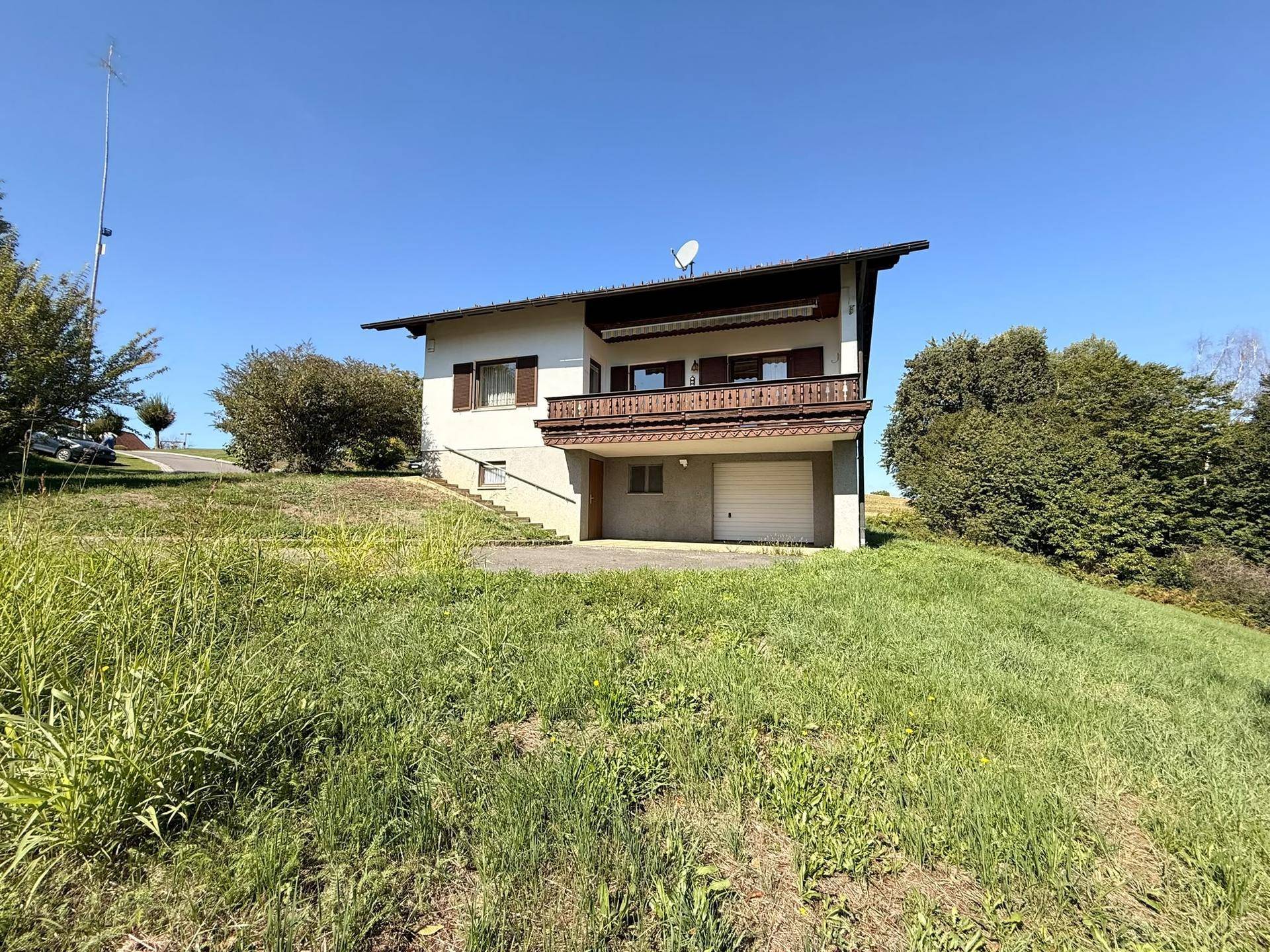 Rückansicht des Hauses mit Balkon, integrierter Garage und weitläufiger Rasenfläche im Vordergrund.