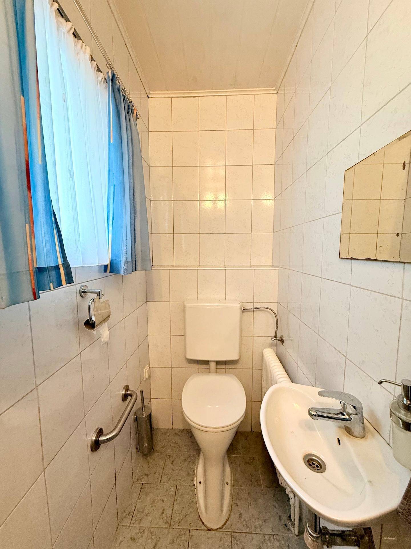 Separate Toilette mit Waschbecken und gefliesten Wänden, ausgestattet mit einem kleinen Fenster.