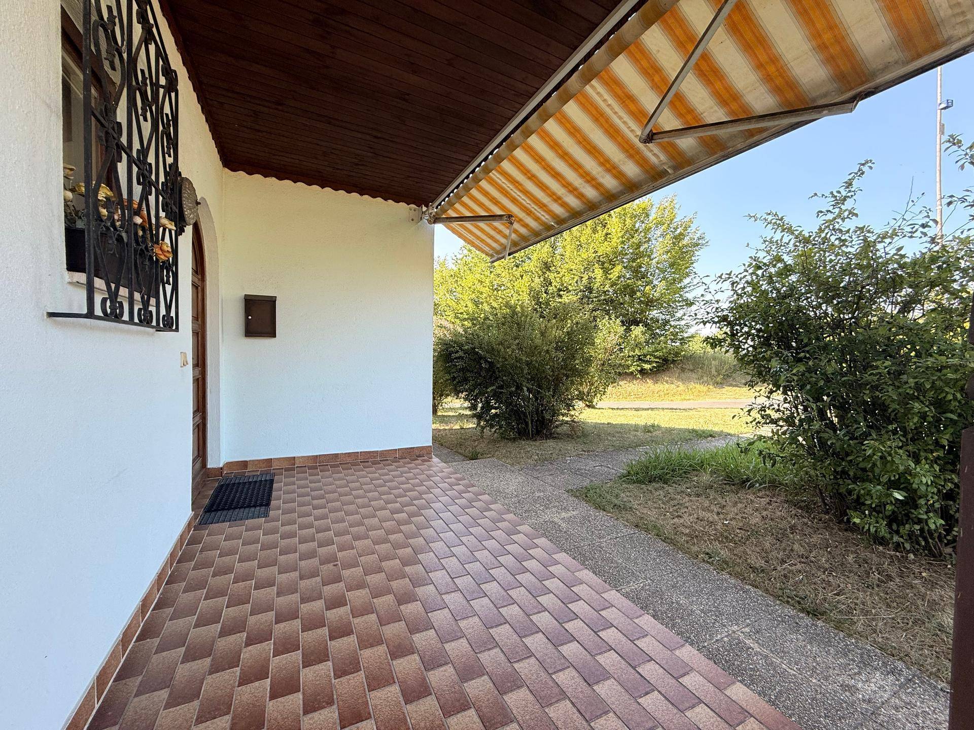Eingangsbereich mit überdachter Terrasse, Fliesenboden und ausziehbarer Markise.