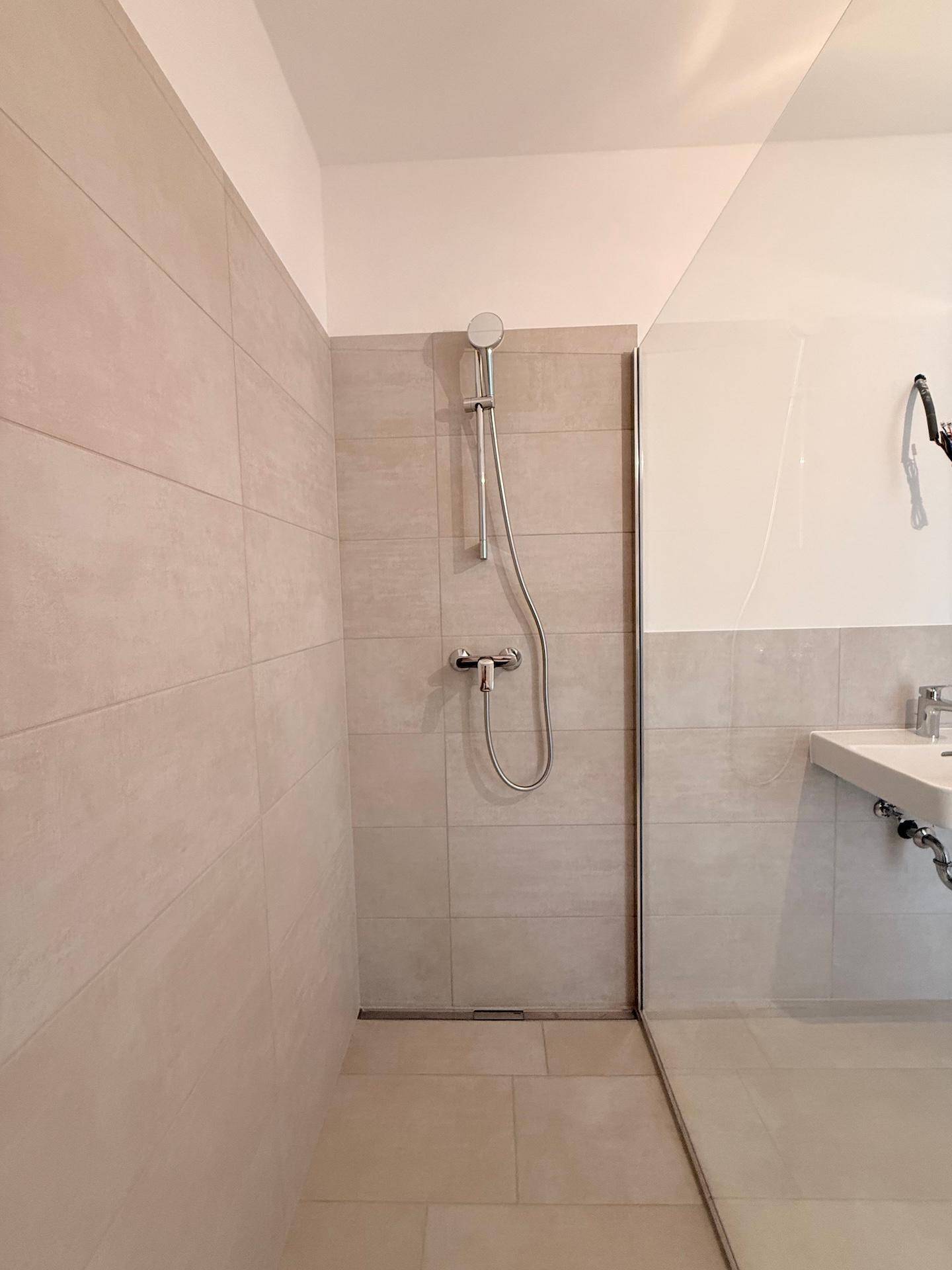Detailansicht der begehbaren Dusche mit Handbrause und modernen Fliesen.
