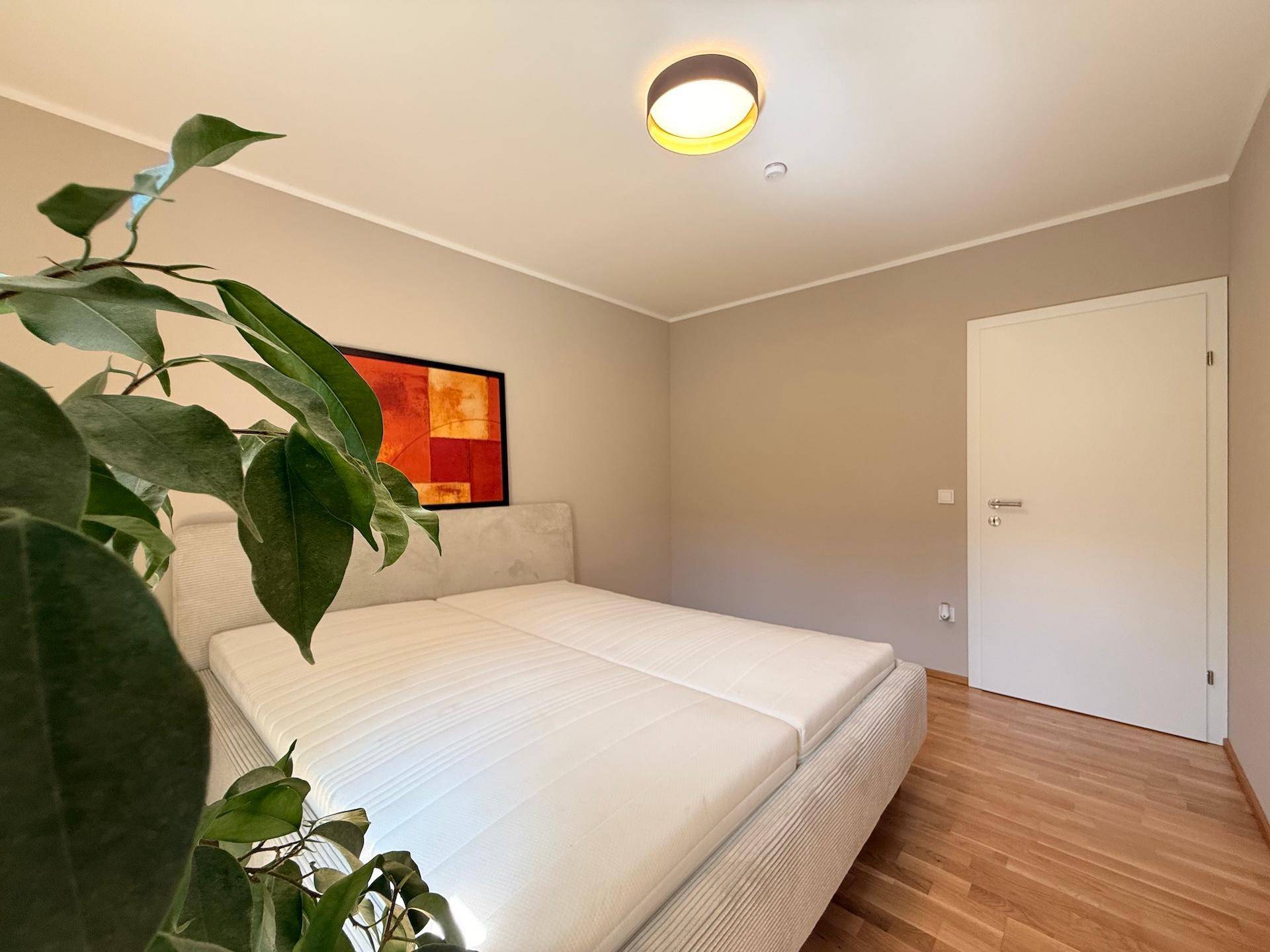 Schlafzimmer mit Doppelbett, Parkettboden und Zugang zu einem weiteren Raum.