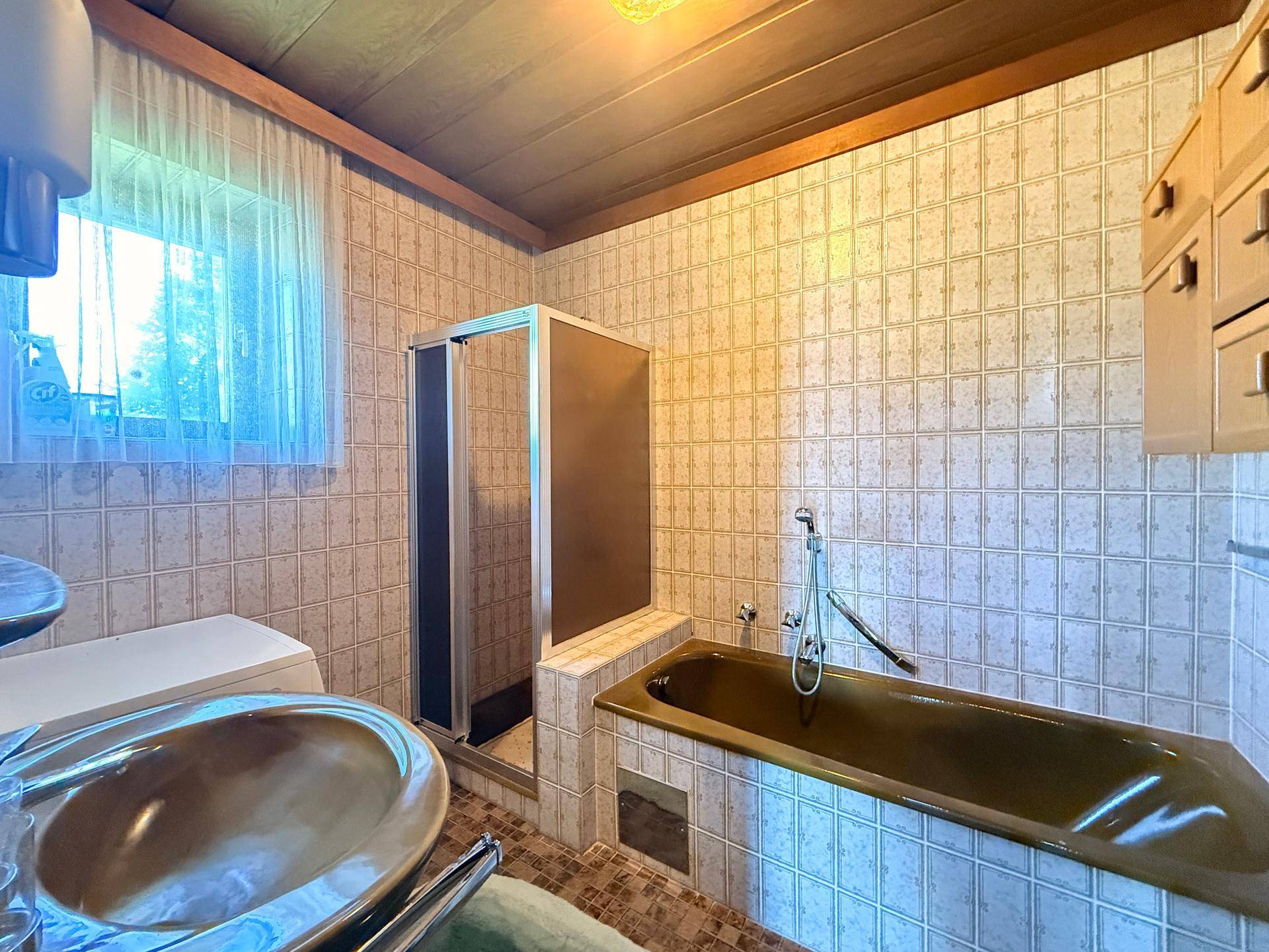Badezimmer im Stil der 80er Jahre mit grüner Badewanne, Dusche und Fliesen an Wänden und Boden.