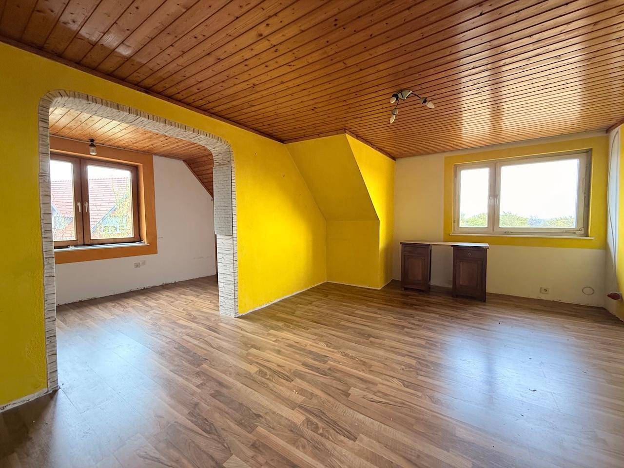 Helles Zimmer im Dachgeschoss mit schrägen Wänden und Laminatboden, bietet Weitblick.