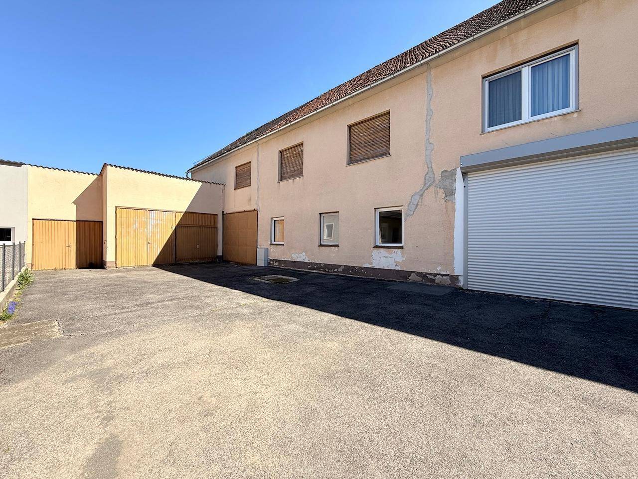 Garagen und Seitenbereich des Hauses mit asphaltiertem Vorplatz unter blauem Himmel.