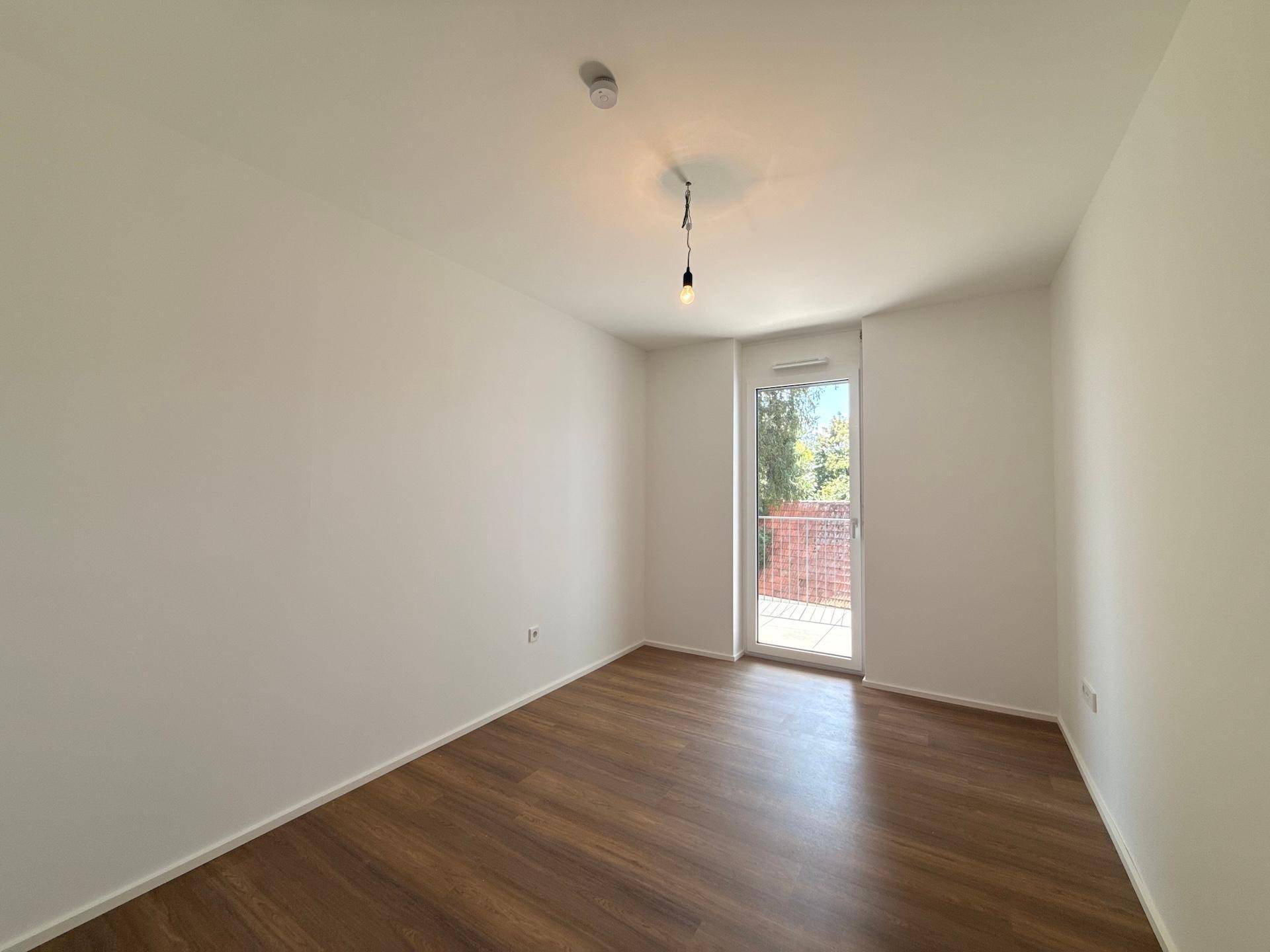 Geräumiges Zimmer mit Holzboden und direktem Zugang zu einem Balkon, sehr hell.