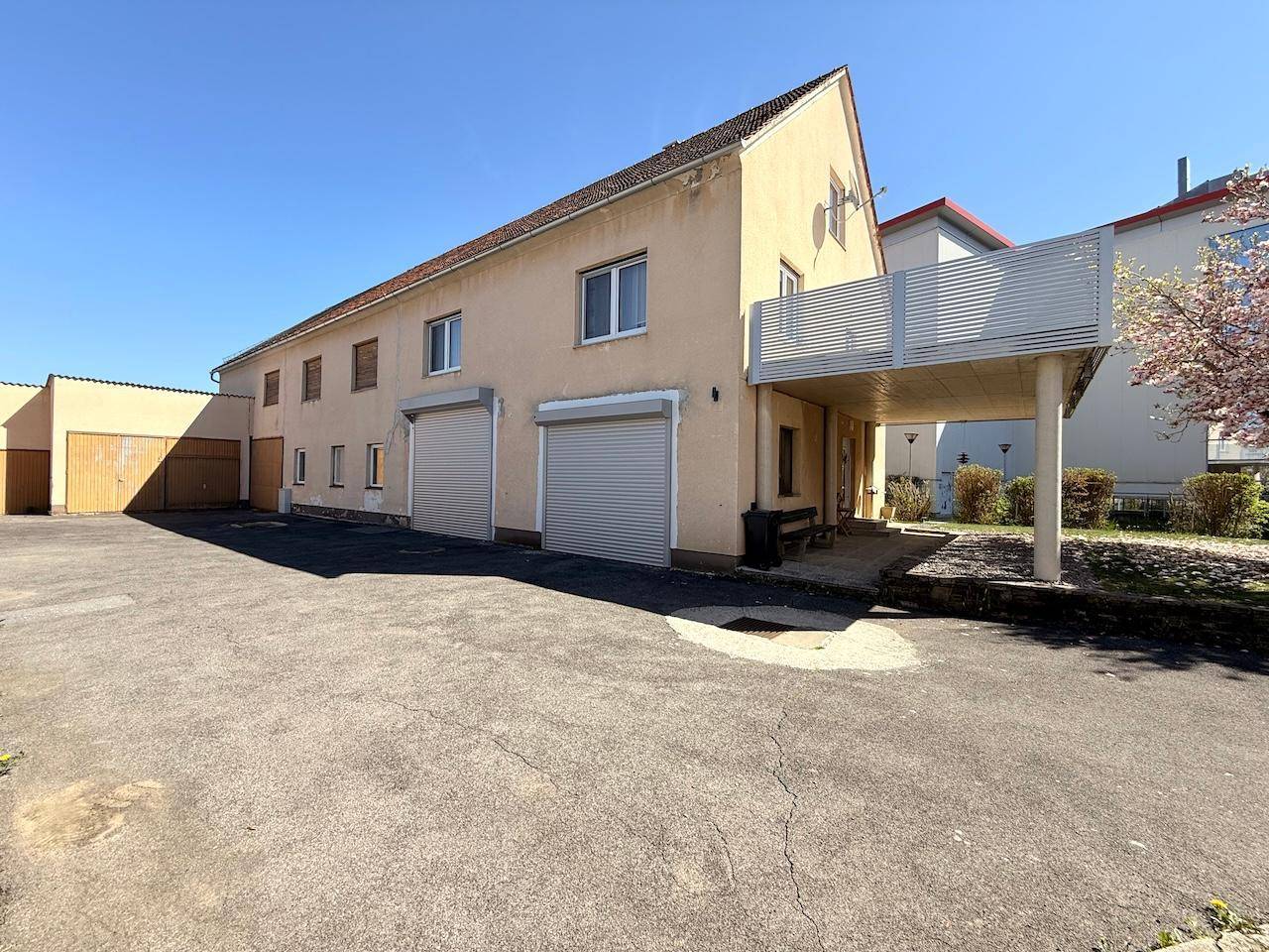 Rückseite des Hauses mit mehreren Garagen und großem asphaltiertem Vorplatz.