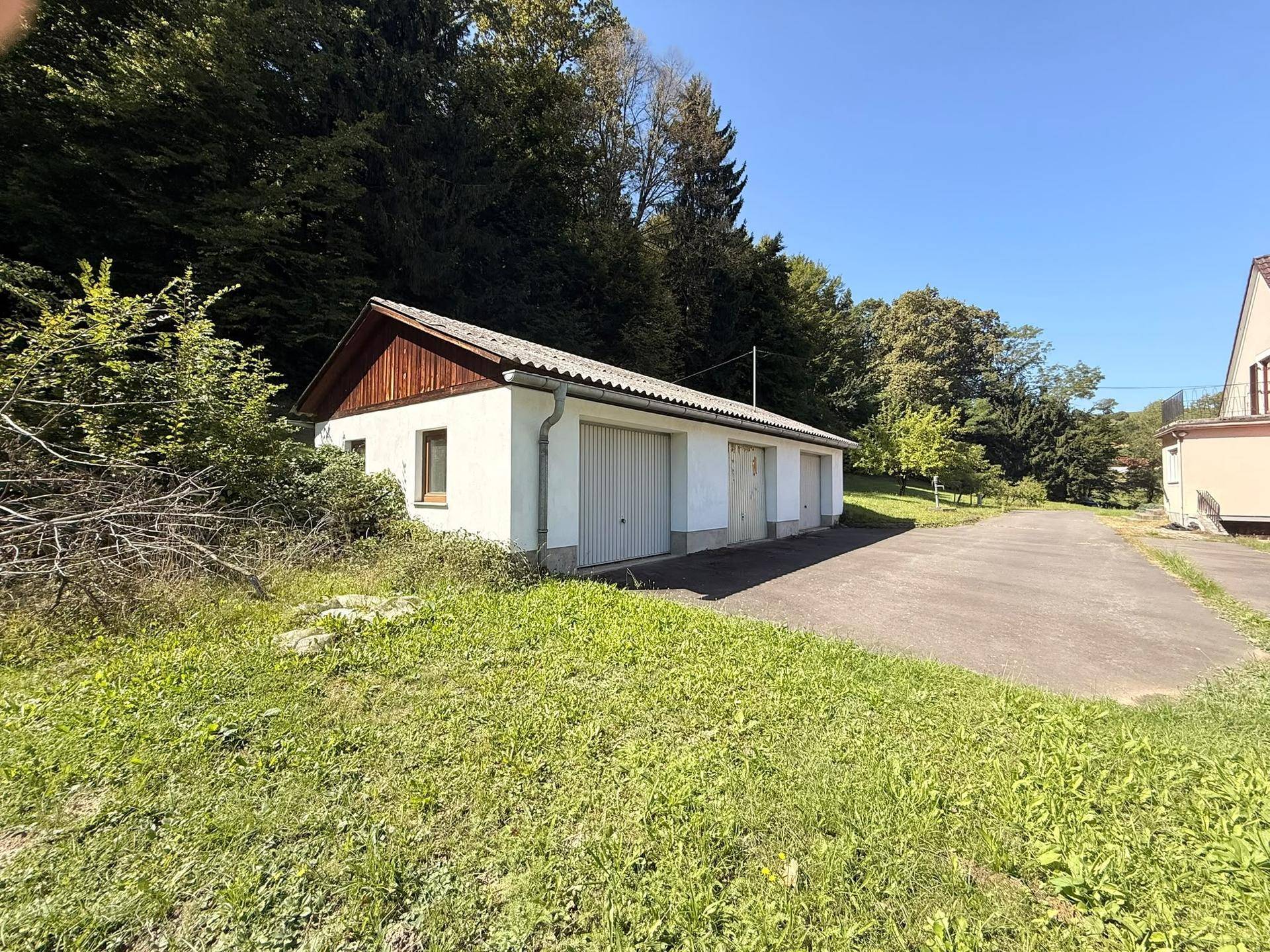 Geräumiges Garagengebäude mit zwei Stellplätzen, umgeben von üppiger Vegetation und Bäumen.