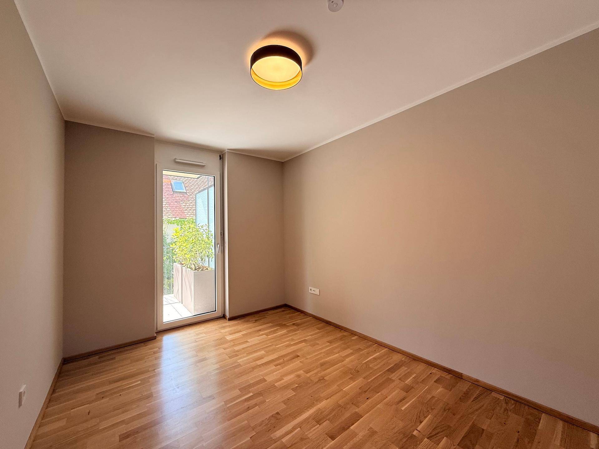 Helles Zimmer mit Parkettboden und Balkontür, ideal als Schlaf- oder Arbeitszimmer.