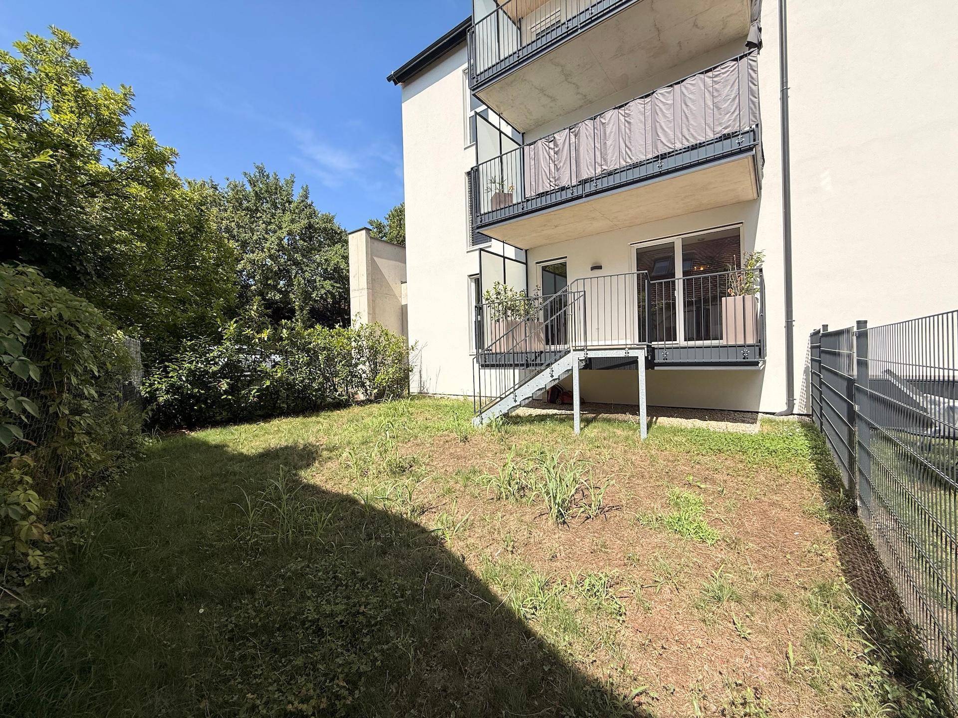 Gartenbereich vor einem modernen Wohngebäude mit Balkonen und üppiger grüner Bepflanzung.