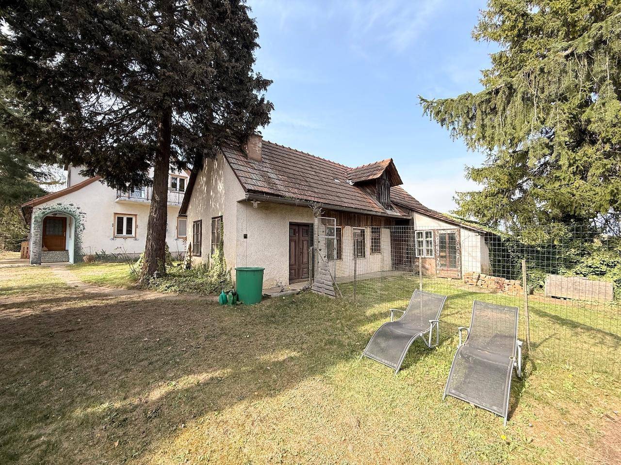 Hinteransicht des Hauses mit Rasenfläche und Liegestühlen im weitläufigen Garten.