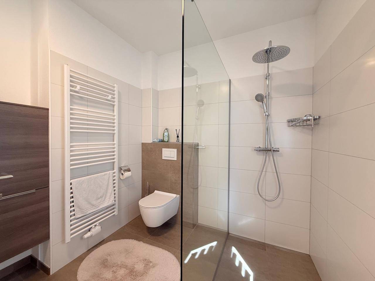 Modernes Badezimmer mit ebenerdiger Dusche, Wand-WC und beheiztem Handtuchhalter.