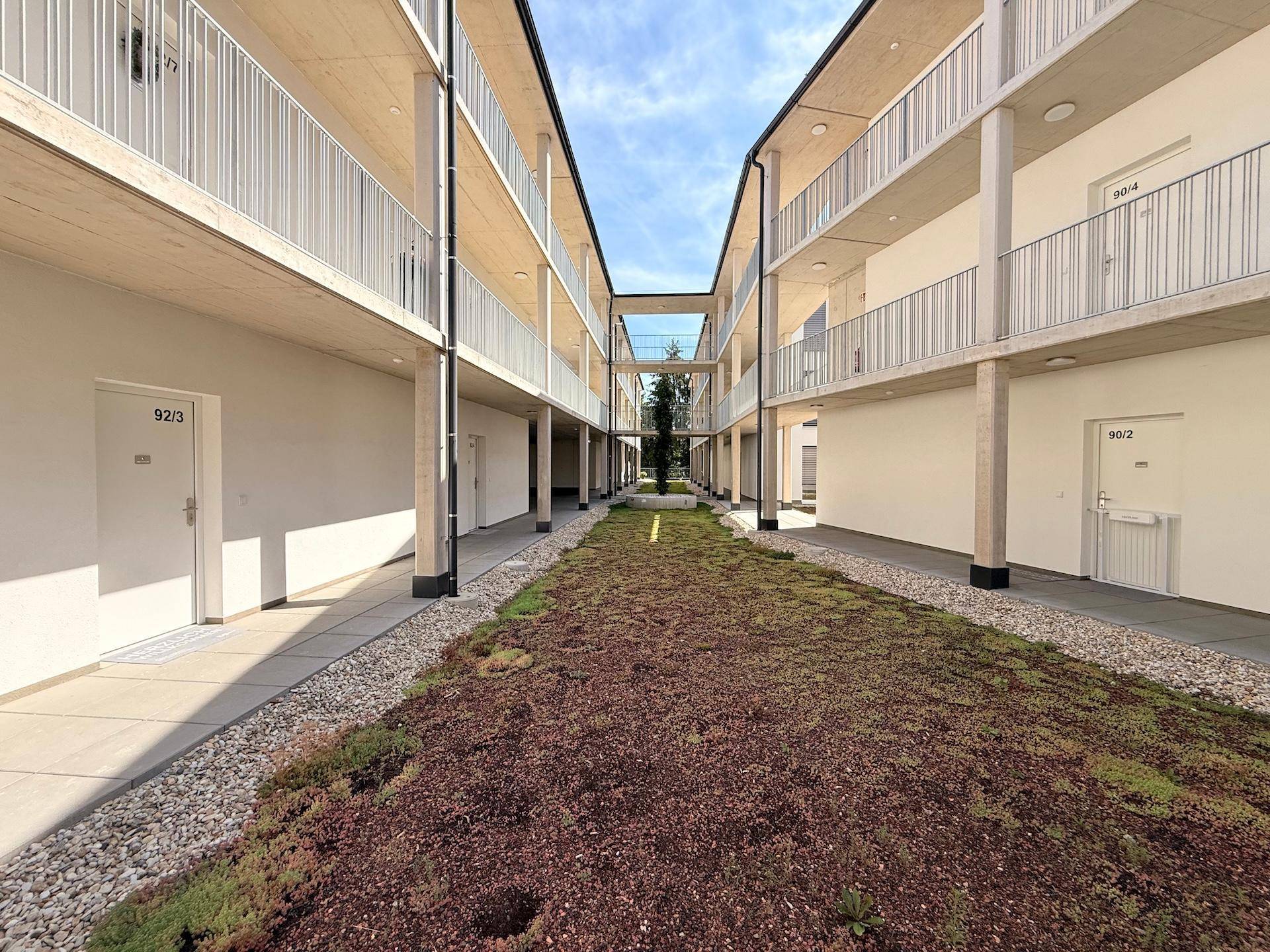 Innenhof eines modernen Wohnkomplexes mit begrünten Flächen und Balkonen.