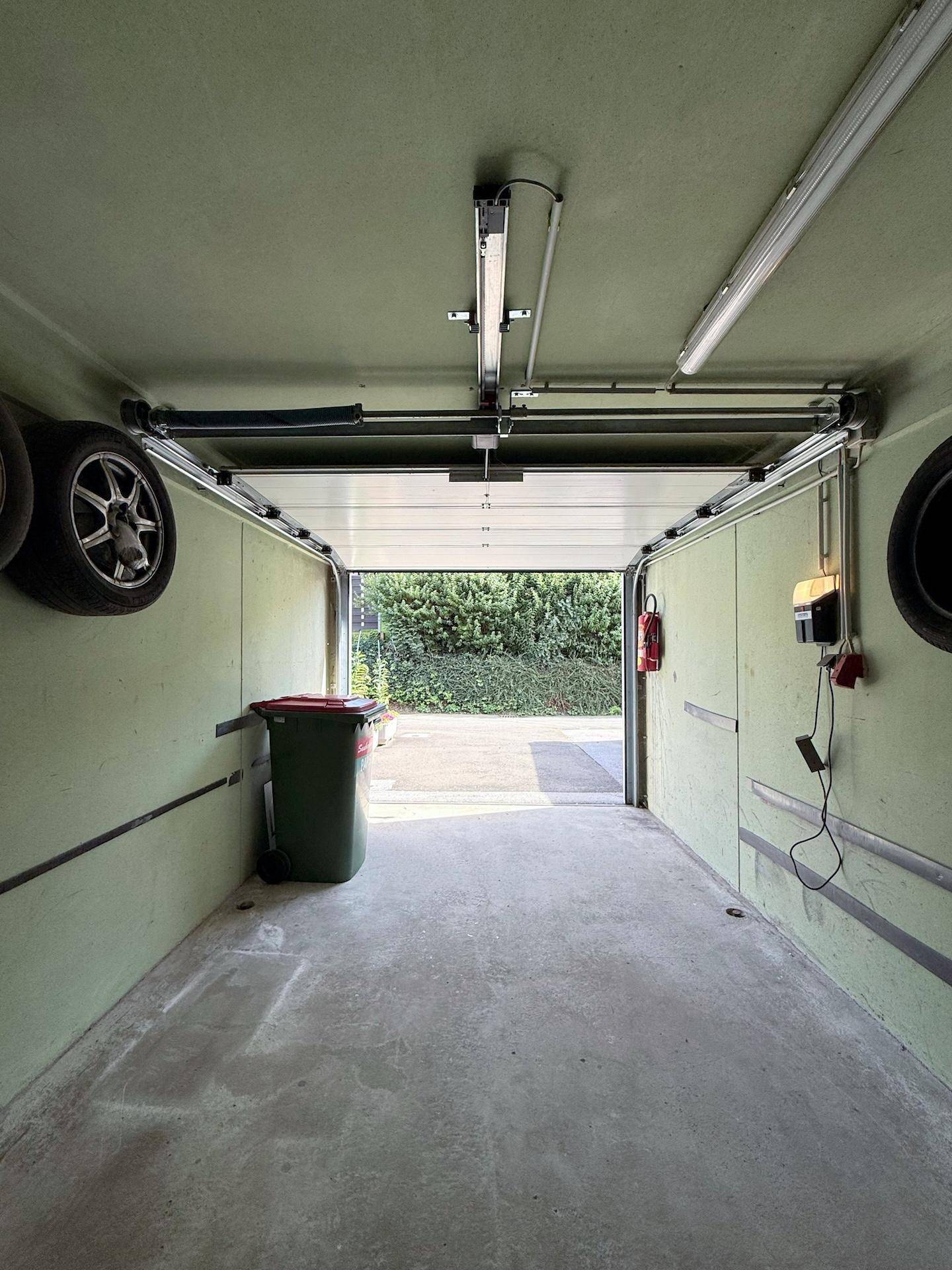 Geräumige Garage mit offenem Tor, Betonboden und Reifen an der Wand.