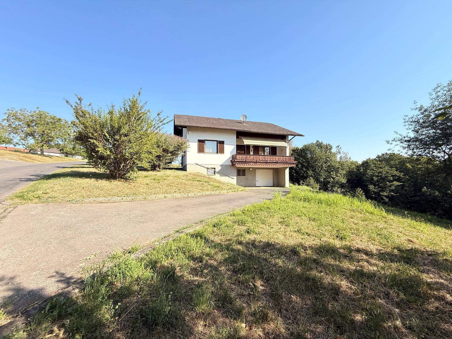 Ansicht des Hauses von vorne mit Balkon, Garage und umgebender grüner Landschaft.