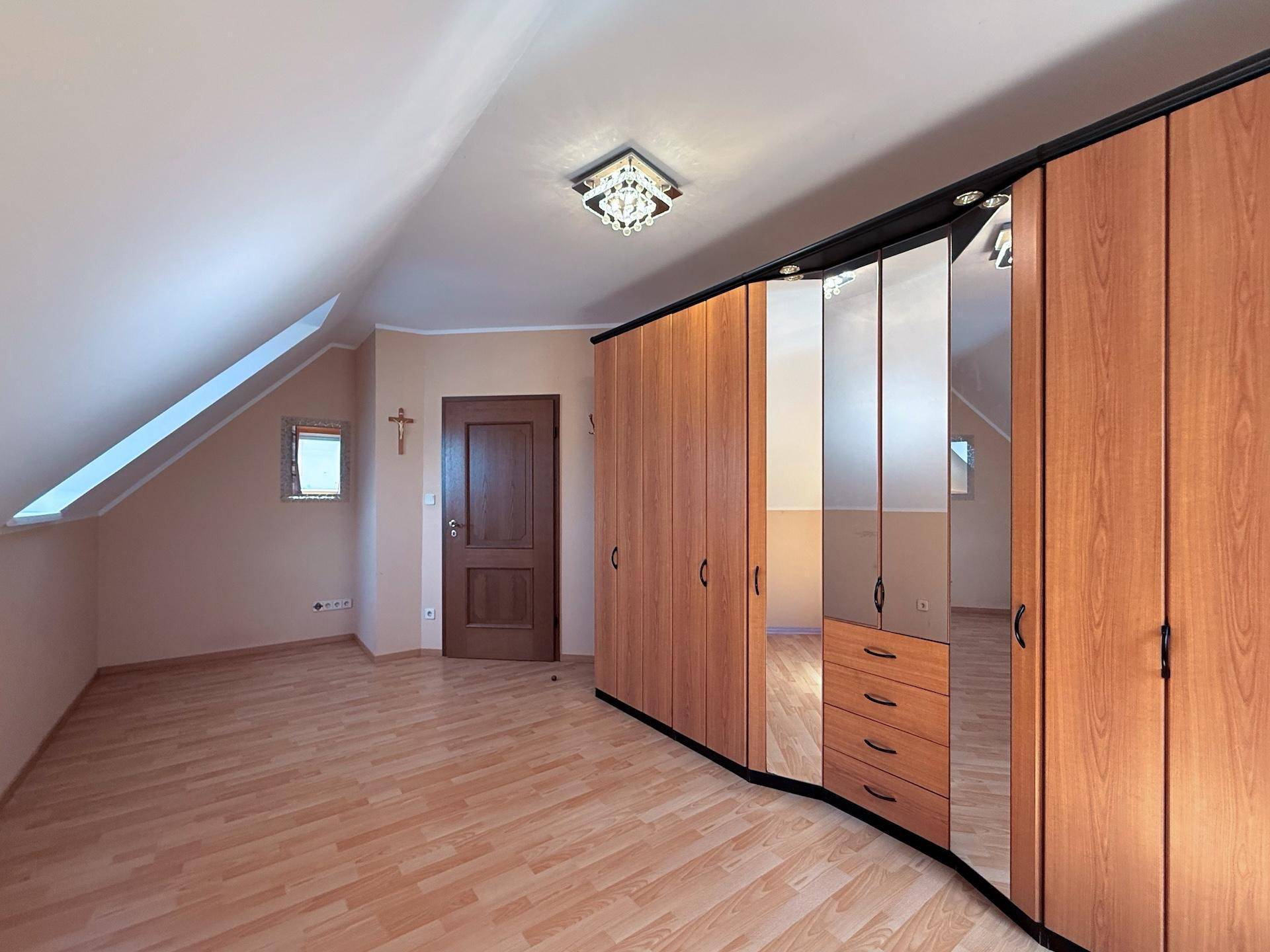 Schlafzimmer mit Dachschräge, Laminatboden und großem Spiegelschrank.