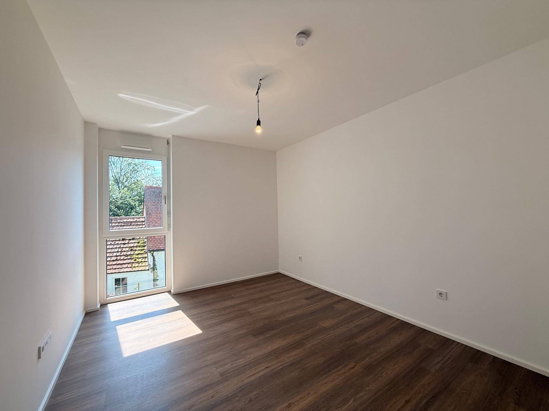 Helles Zimmer mit modernem Holzboden und weiß gestrichenen Wänden, mit Zugang nach draußen.