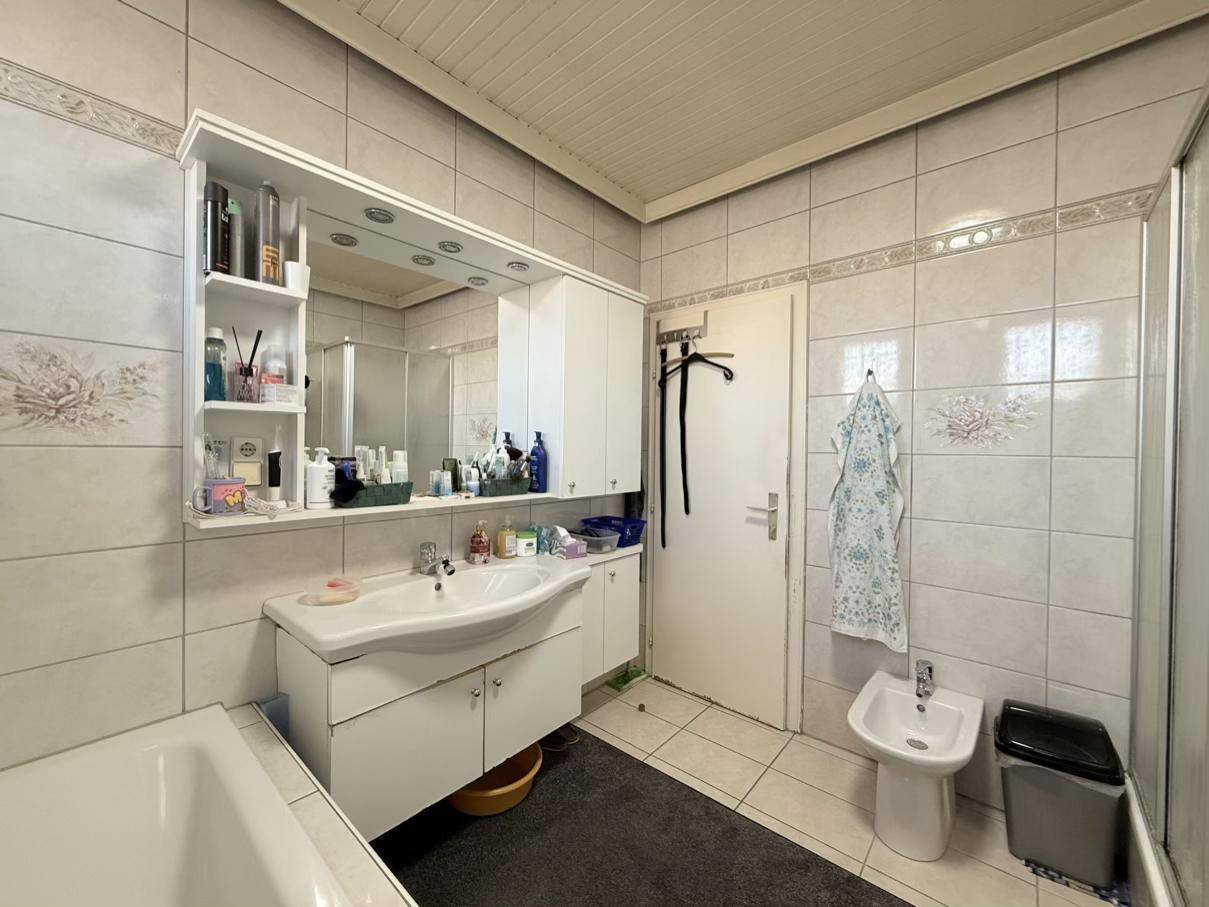 Gefliestes Badezimmer mit Waschbecken, Spiegelschrank und Bidet, gut beleuchtet.