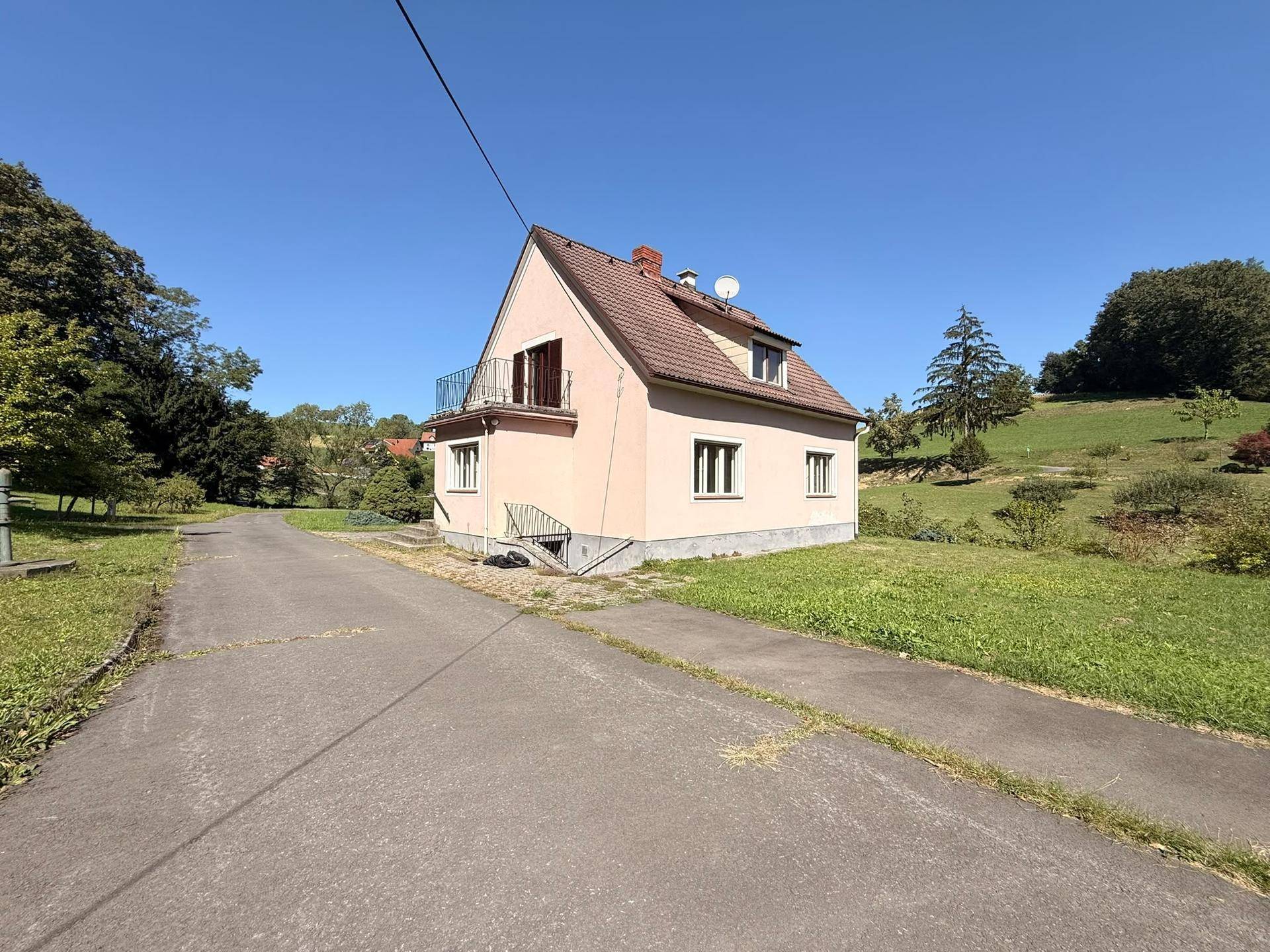 Einfamilienhaus mit Balkon und gepflegtem Grundstück, umgeben von ländlicher Idylle.