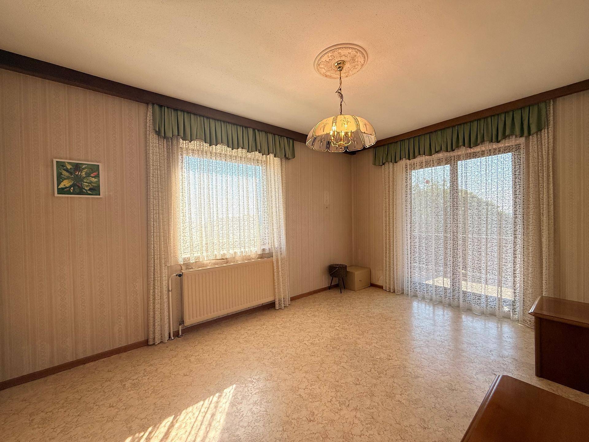 Helles Schlafzimmer mit gemusterter Tapete, großem Fenster und direktem Zugang zum Balkon.