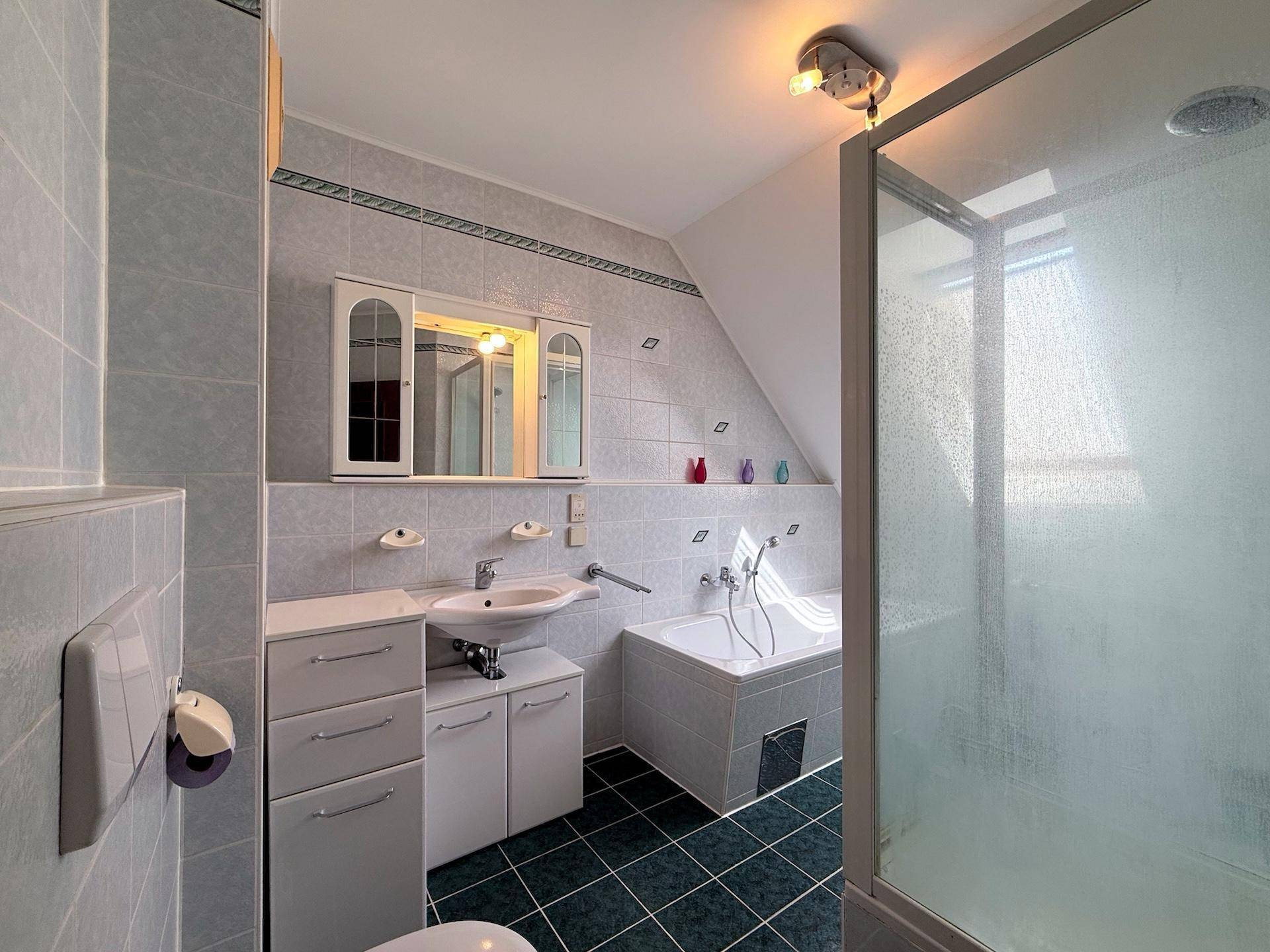 Badezimmer mit Badewanne, Duschkabine, Waschbecken und Dachschräge.