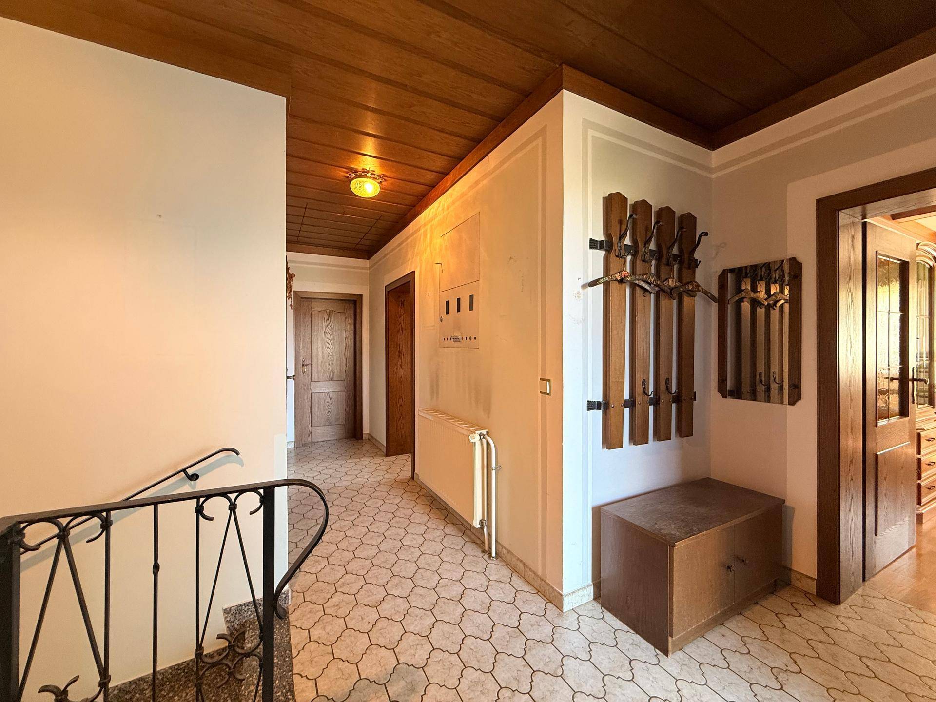 Flur mit gemusterten Fliesen, Holzdecke und einer Garderobe, die zu weiteren Räumen führt.