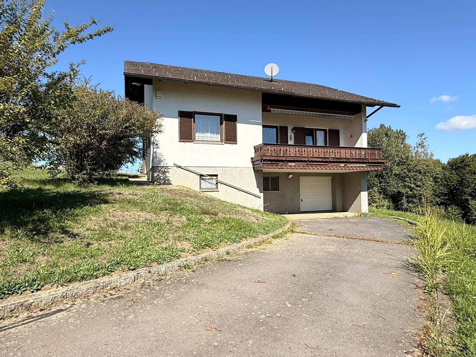 Das Haus präsentiert sich mit einem Balkon und einer integrierten Garage, umgeben von viel Grün.