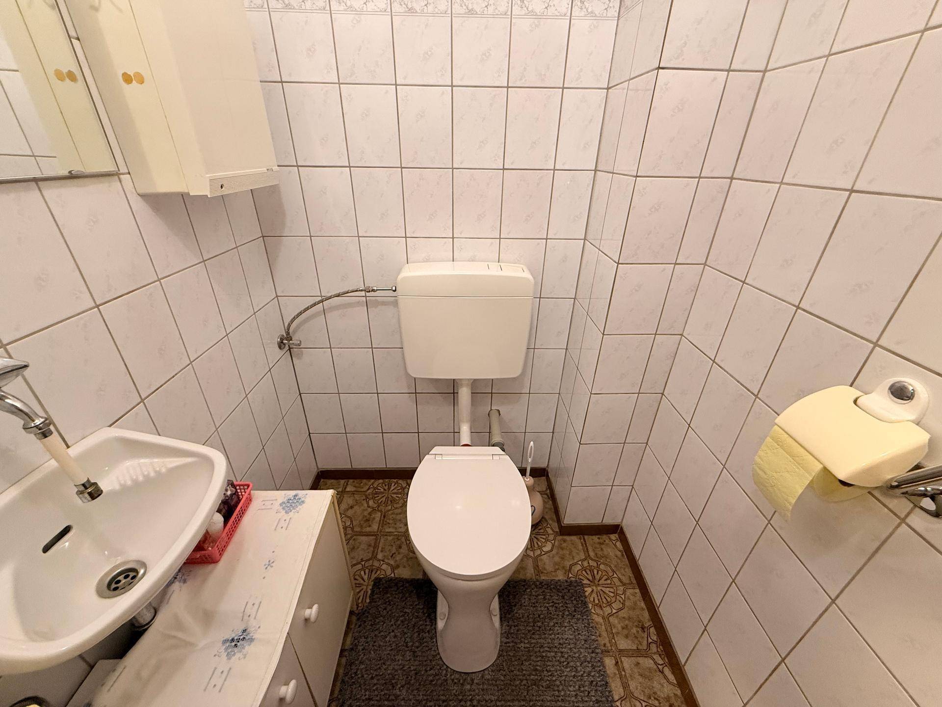 Kleines Gäste-WC mit Toilette, Waschbecken und weißen Fliesen an den Wänden.