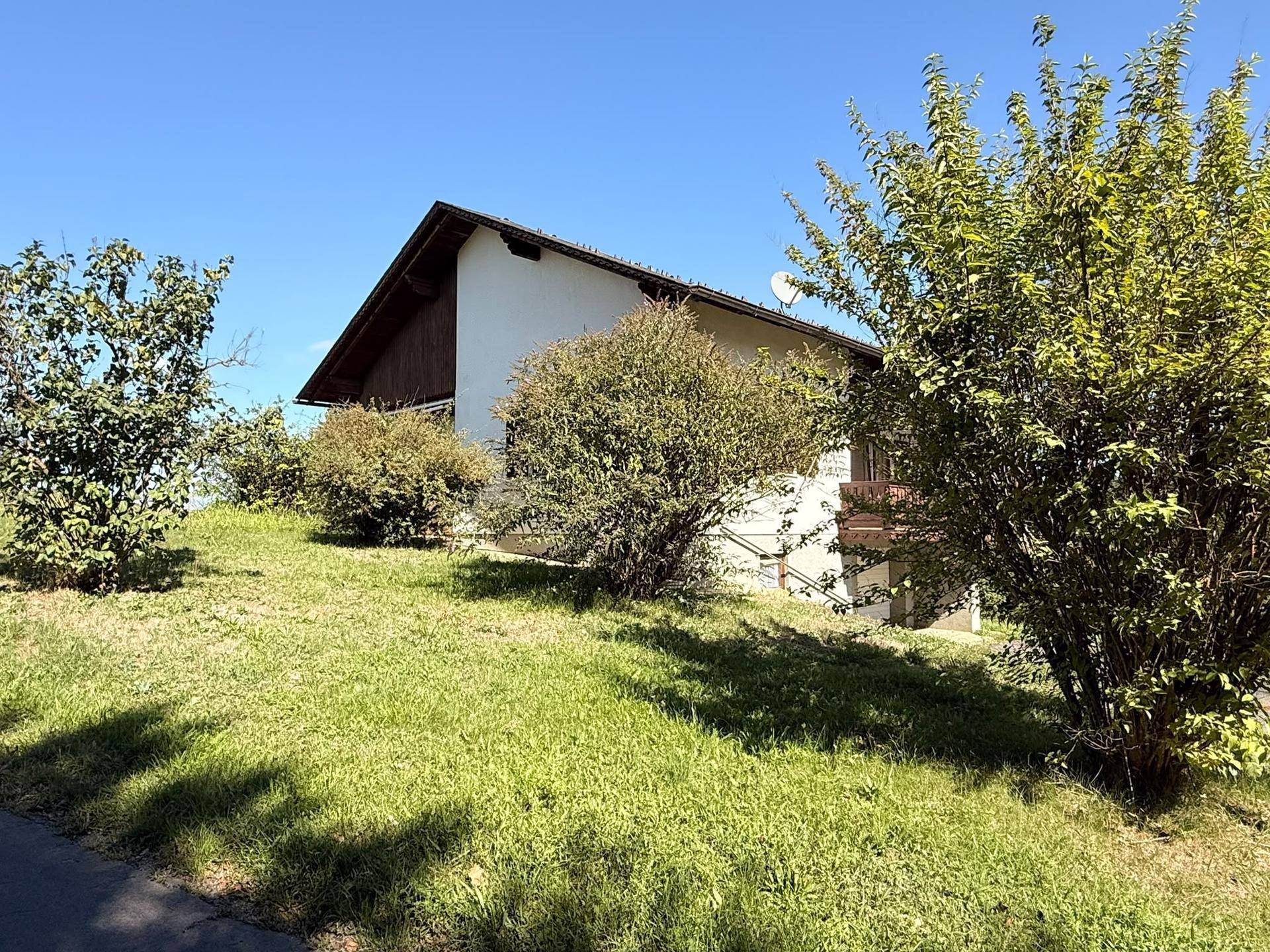 Das Haus ist von üppigem Grün umgeben, mit Sträuchern und Rasenflächen im Vordergrund.