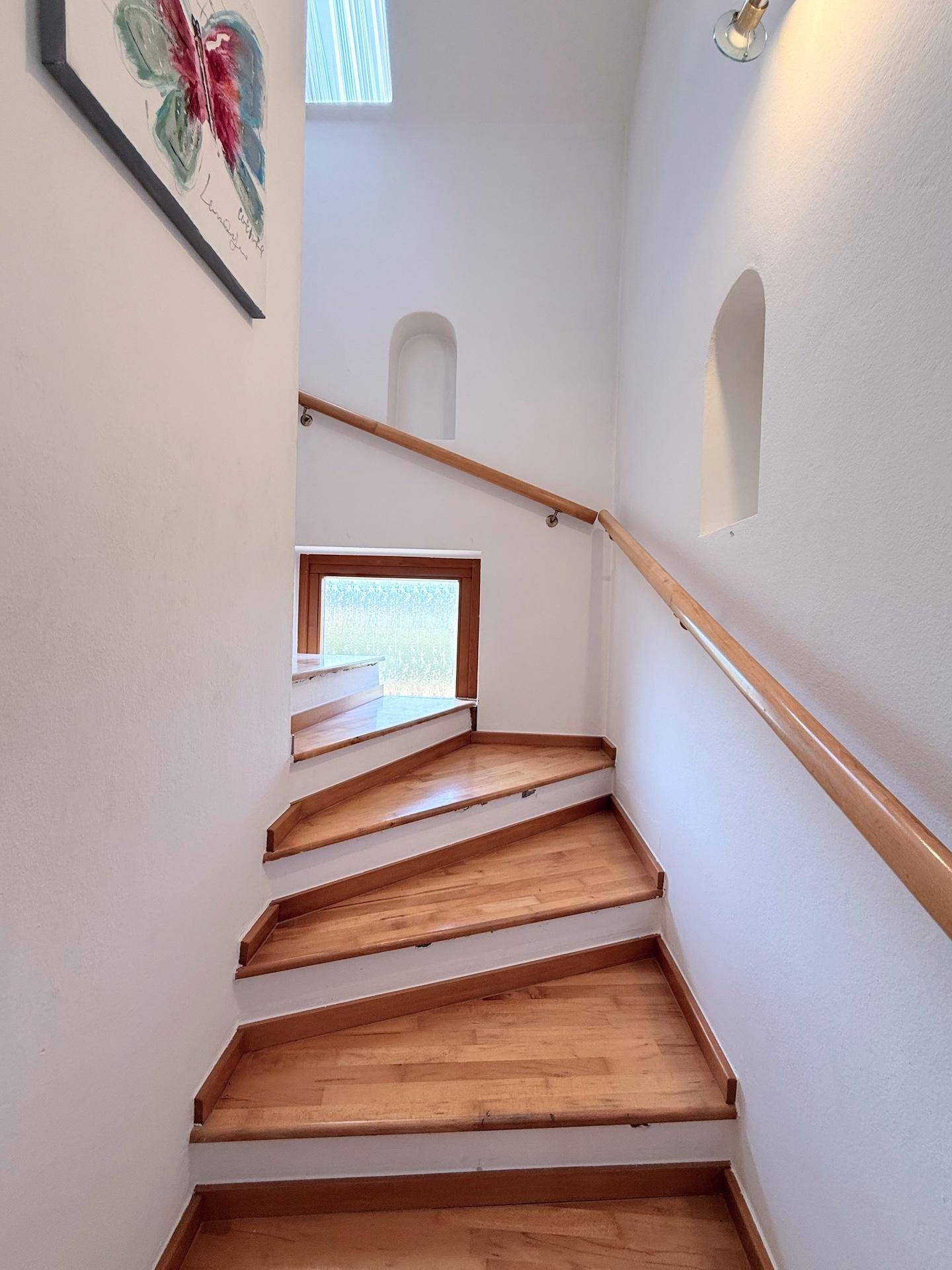 Holztreppe mit Handlauf und kleinen Nischen in einem hellen Treppenhaus.