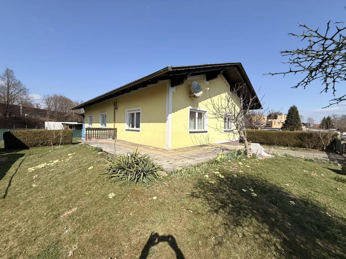 Gelbes Haus mit gepflasterter Fläche neben dem Gebäude und einem grünen Rasenbereich an einem sonnigen Tag.