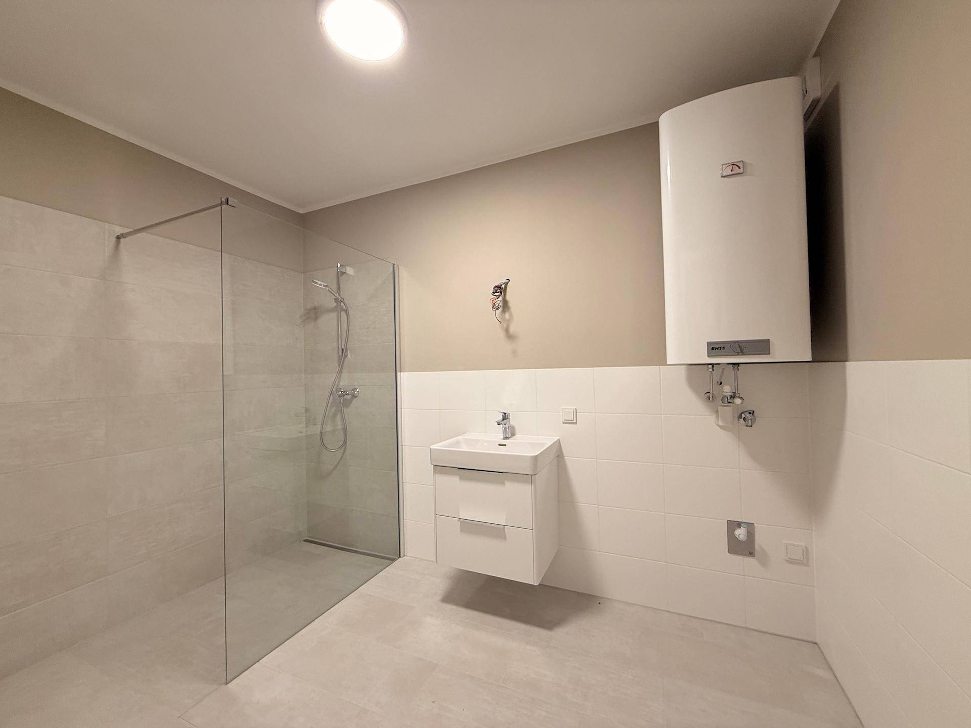 Geräumiges Badezimmer mit ebenerdiger Dusche, Waschbecken und Warmwasserboiler.