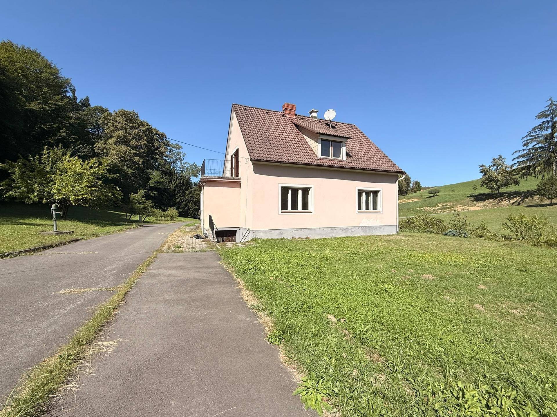 Rückansicht des Hauses mit Satteldach, umgeben von weitläufigen Grünflächen und Bäumen.