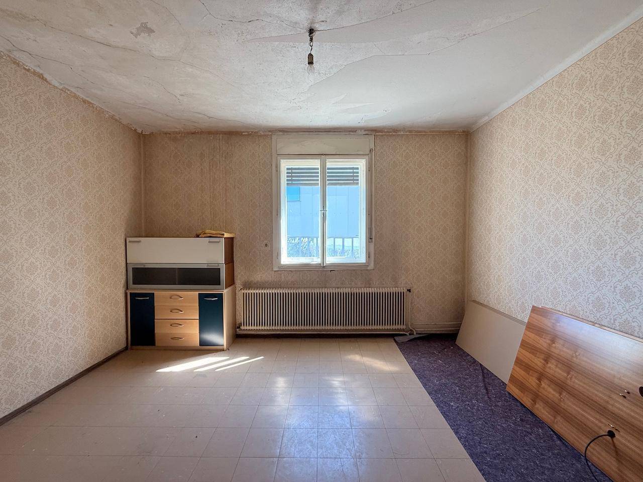 Leerer Raum mit älterer Tapete und Fliesenboden, der eine Renovierung benötigt.