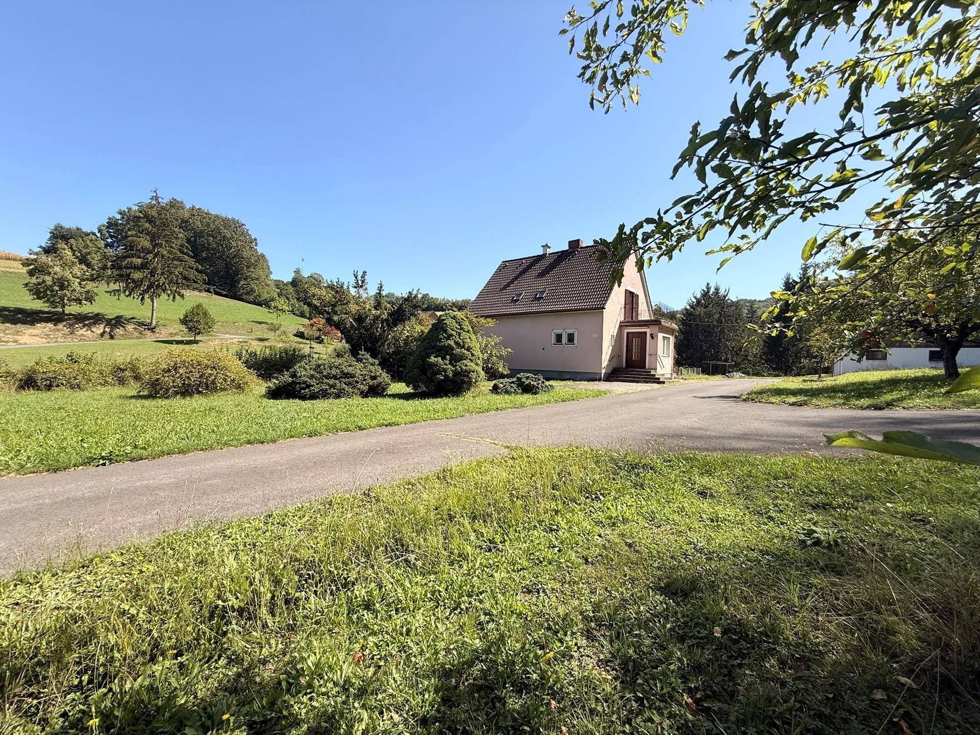 Einfamilienhaus in ländlicher Umgebung mit viel Grün und klarem blauen Himmel.