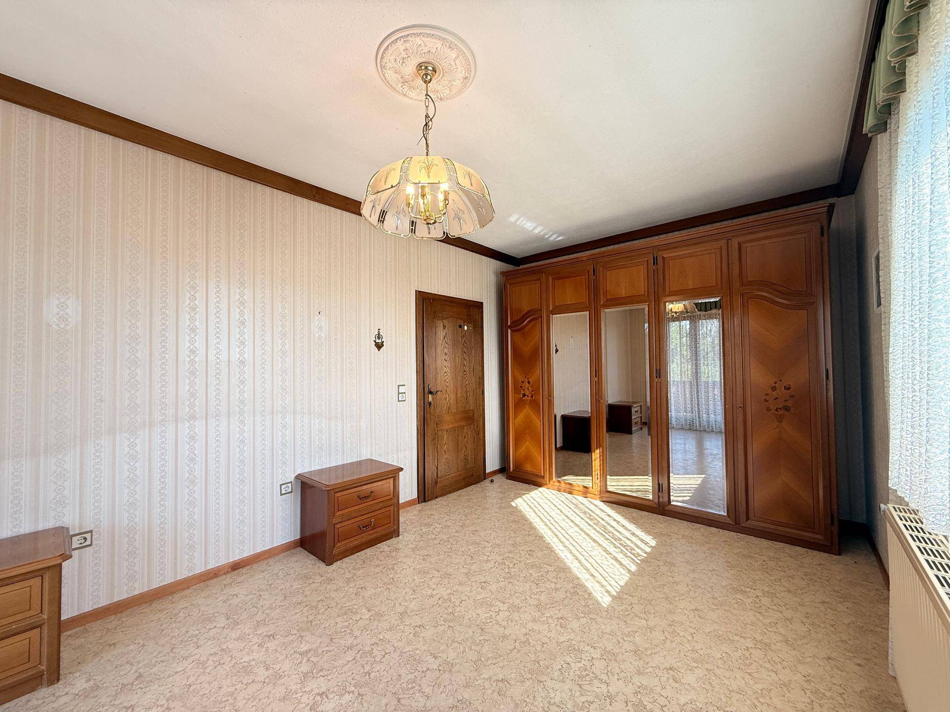 Geräumiges Schlafzimmer mit großem Holzschrank, gemusterter Tapete und viel natürlichem Licht.