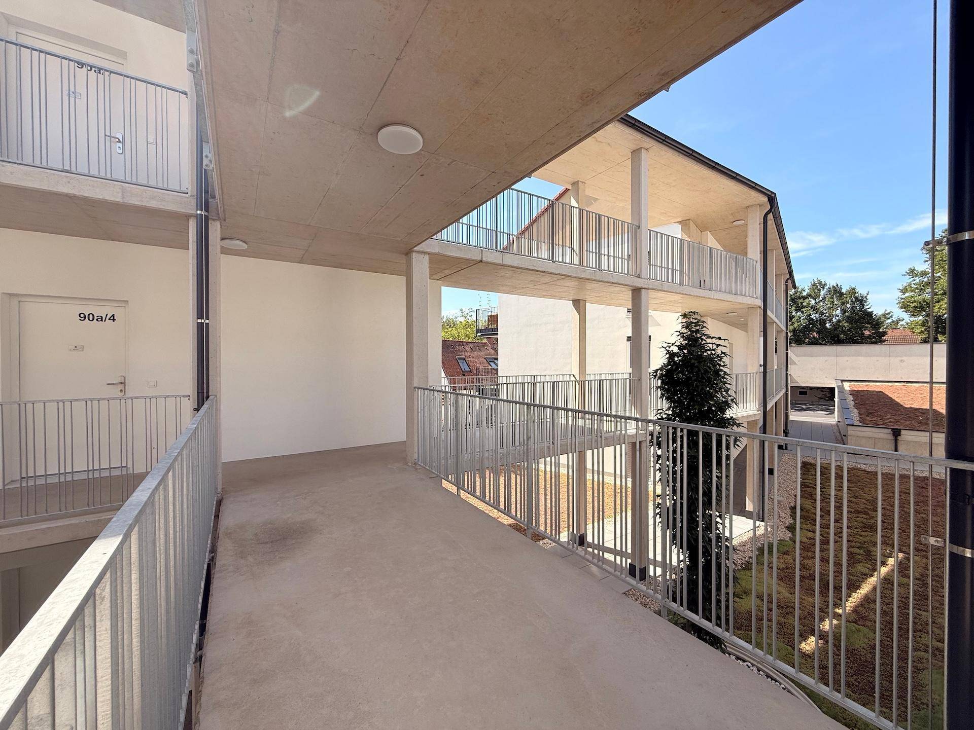 Überdachter Außenflur im Obergeschoss eines modernen Wohnkomplexes mit Blick in den Innenhof.