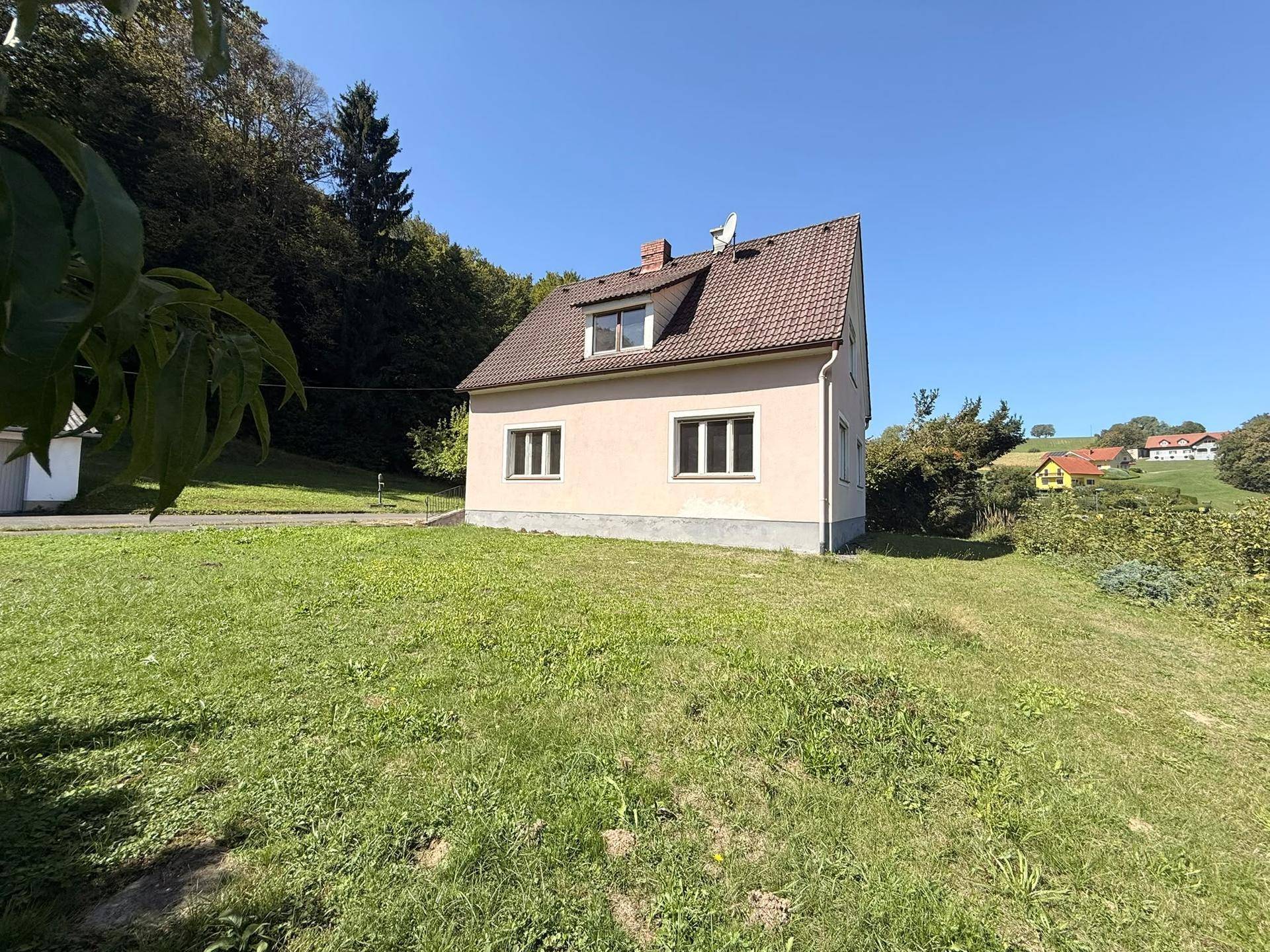 Rückansicht des Einfamilienhauses mit gepflegtem Rasen und Blick auf die umliegende Hügellandschaft.