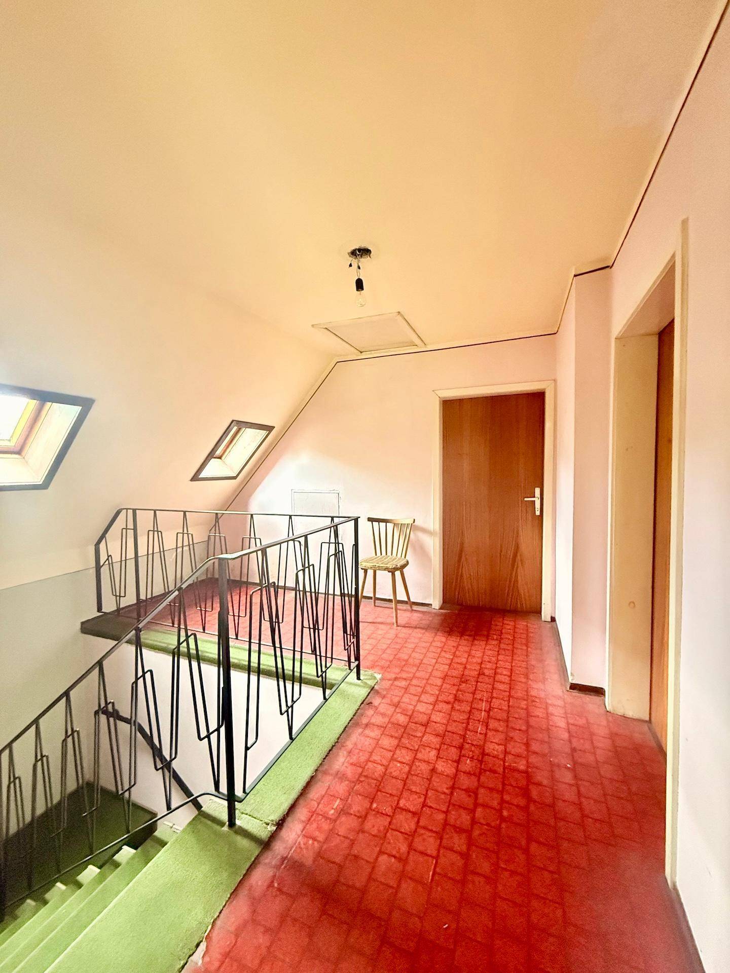 Flur im Obergeschoss mit Teppichboden, Holztreppe und Dachfenstern, die natürliches Licht hereinlassen.
